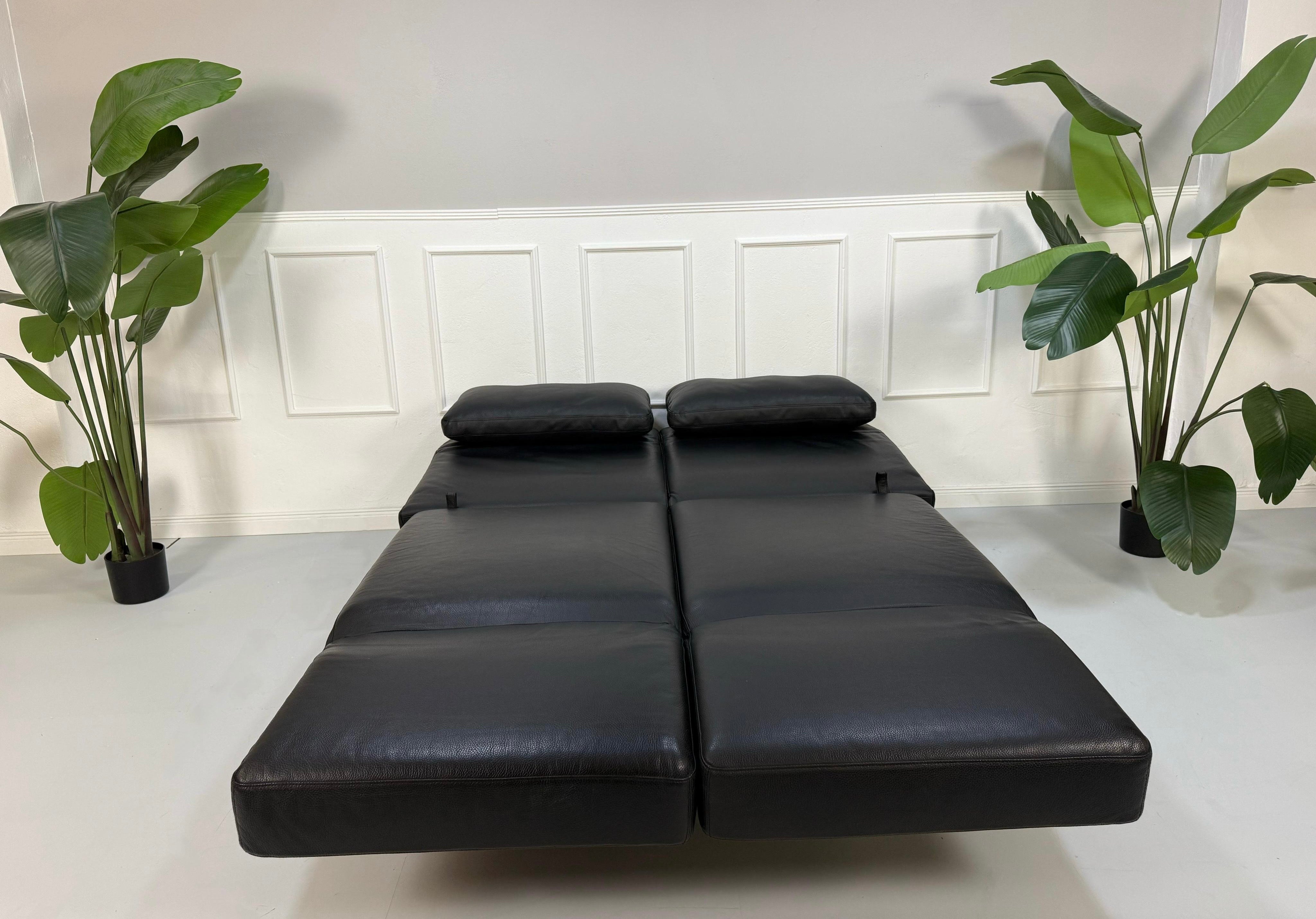 Gebrauchtes schwarzes Brühl Moule Designer Leder Sofa vor einer Wand, stilvoll und modern eingerichtet.