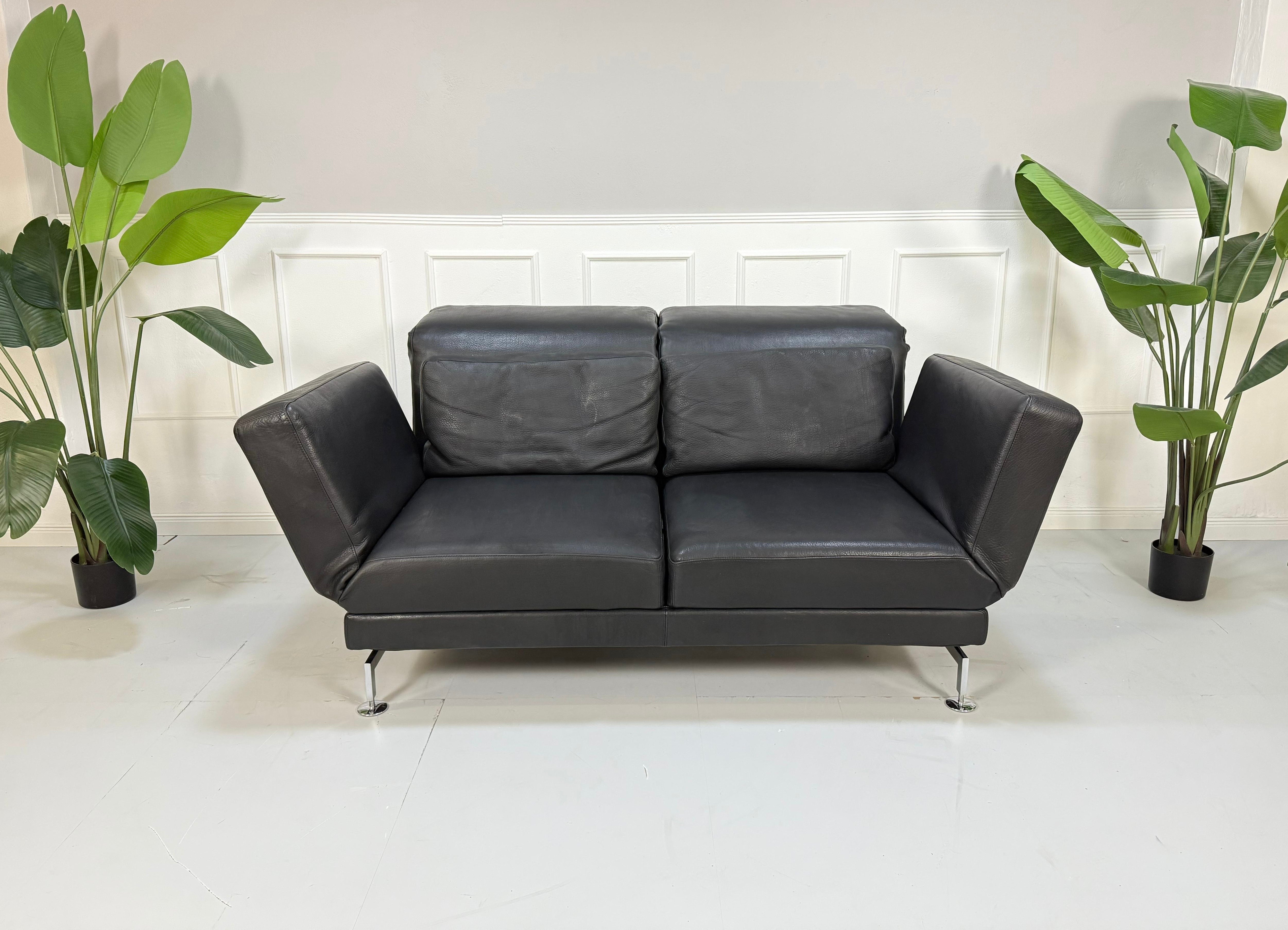 Gebrauchtes schwarzes Brühl Moule Designer Leder Sofa vor einer Wand, stilvoll und modern eingerichtet.