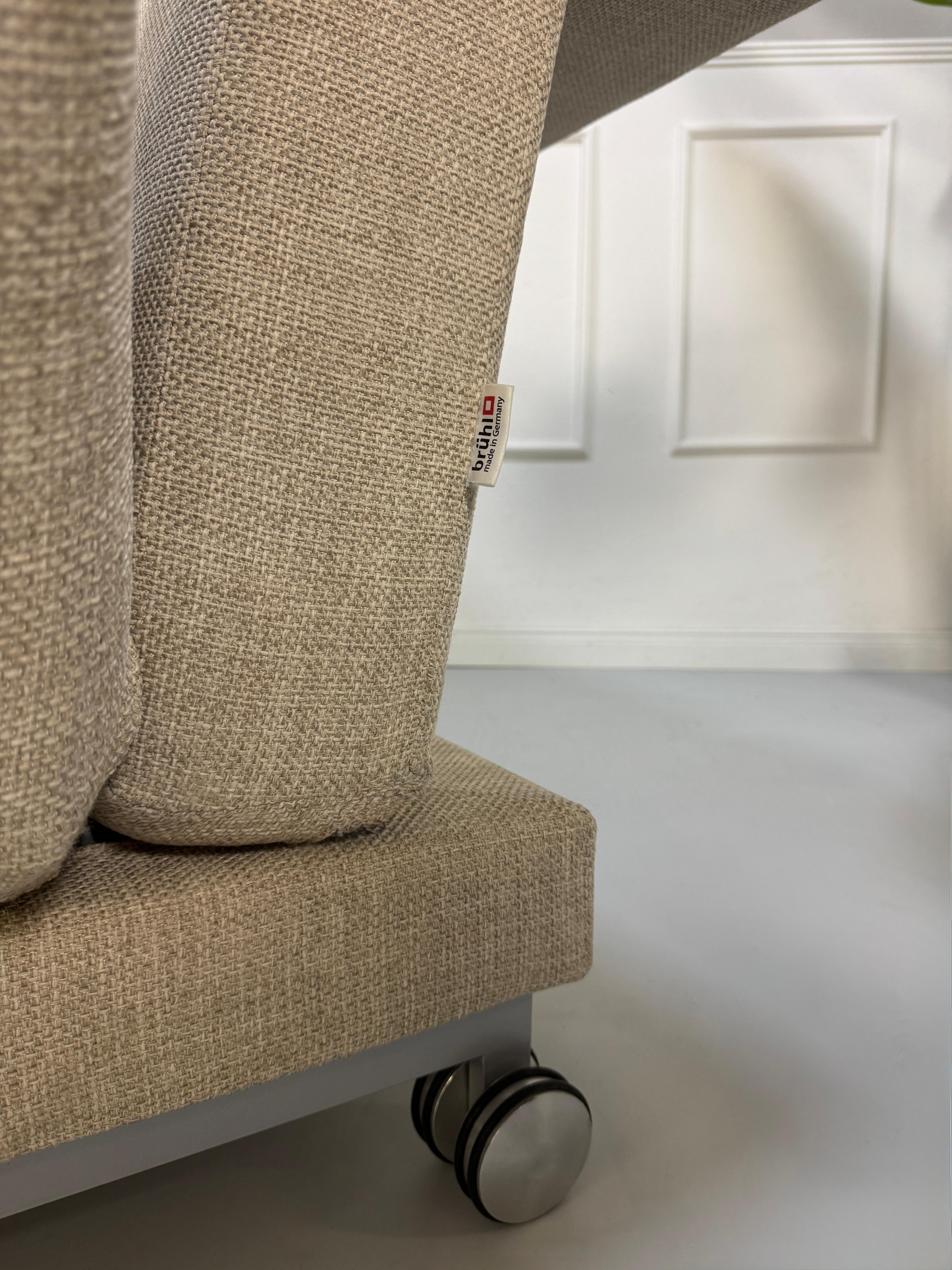 Gebrauchtes beiges Brühl Moule Designer Stoff Sofa vor einer Wand, stilvoll und modern eingerichtet.