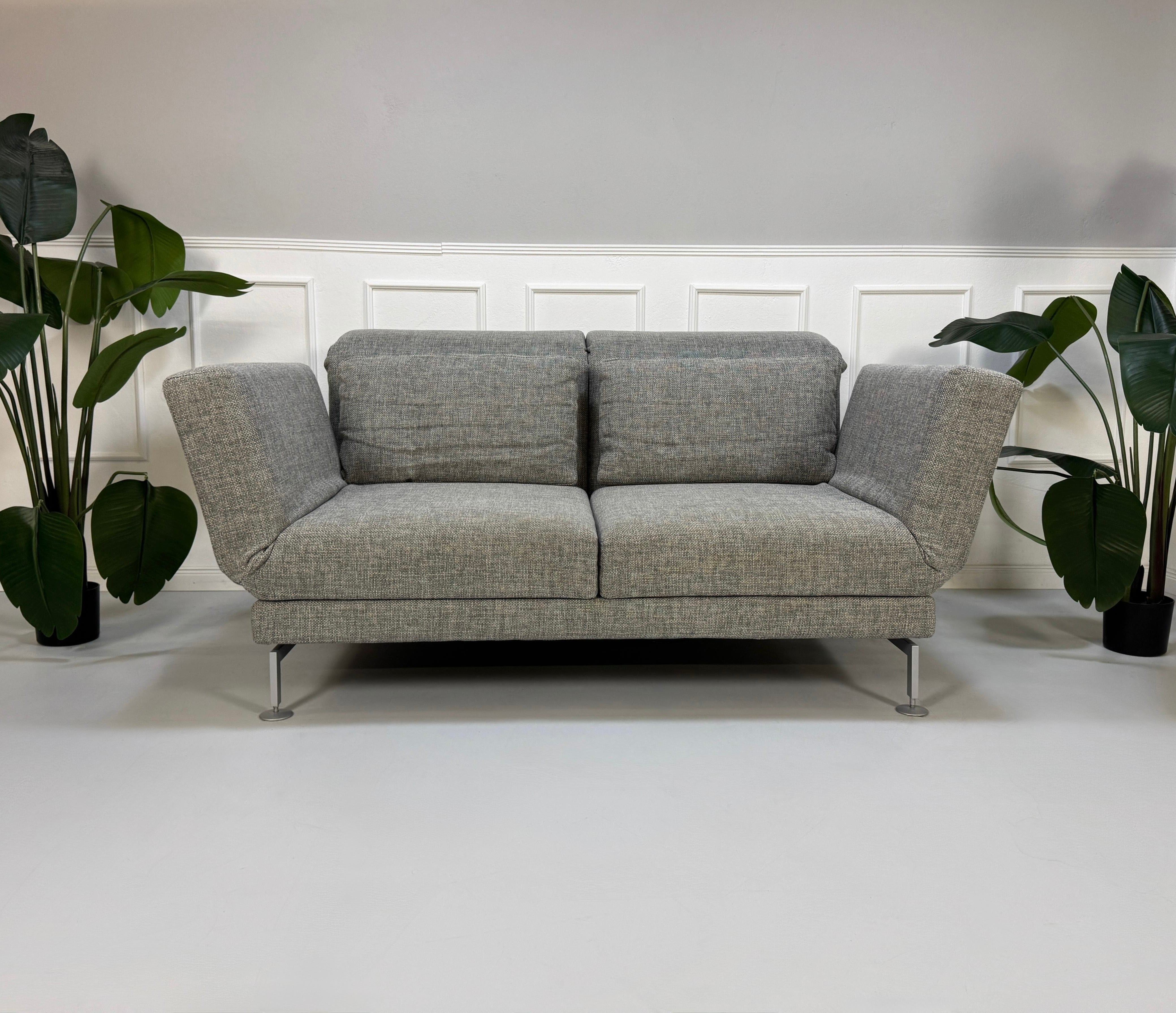 Refurbished graues Brühl Moule Designer Stoff Sofa vor einer Wand, stilvoll und modern eingerichtet.