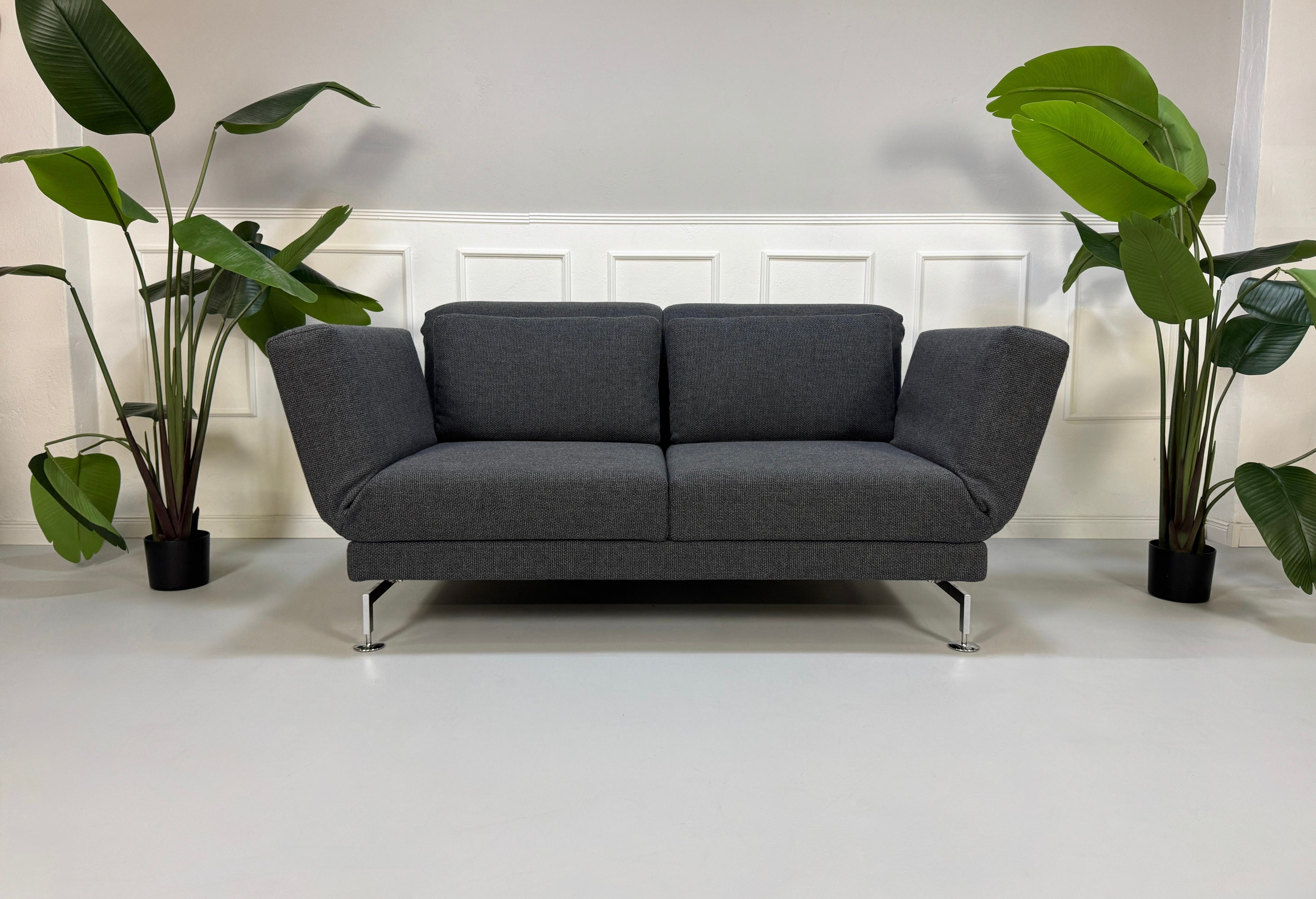 Graues Ausstellungsstück Brühl Moule Designer Stoff Sofa vor einer Wand, stilvoll und modern eingerichtet.