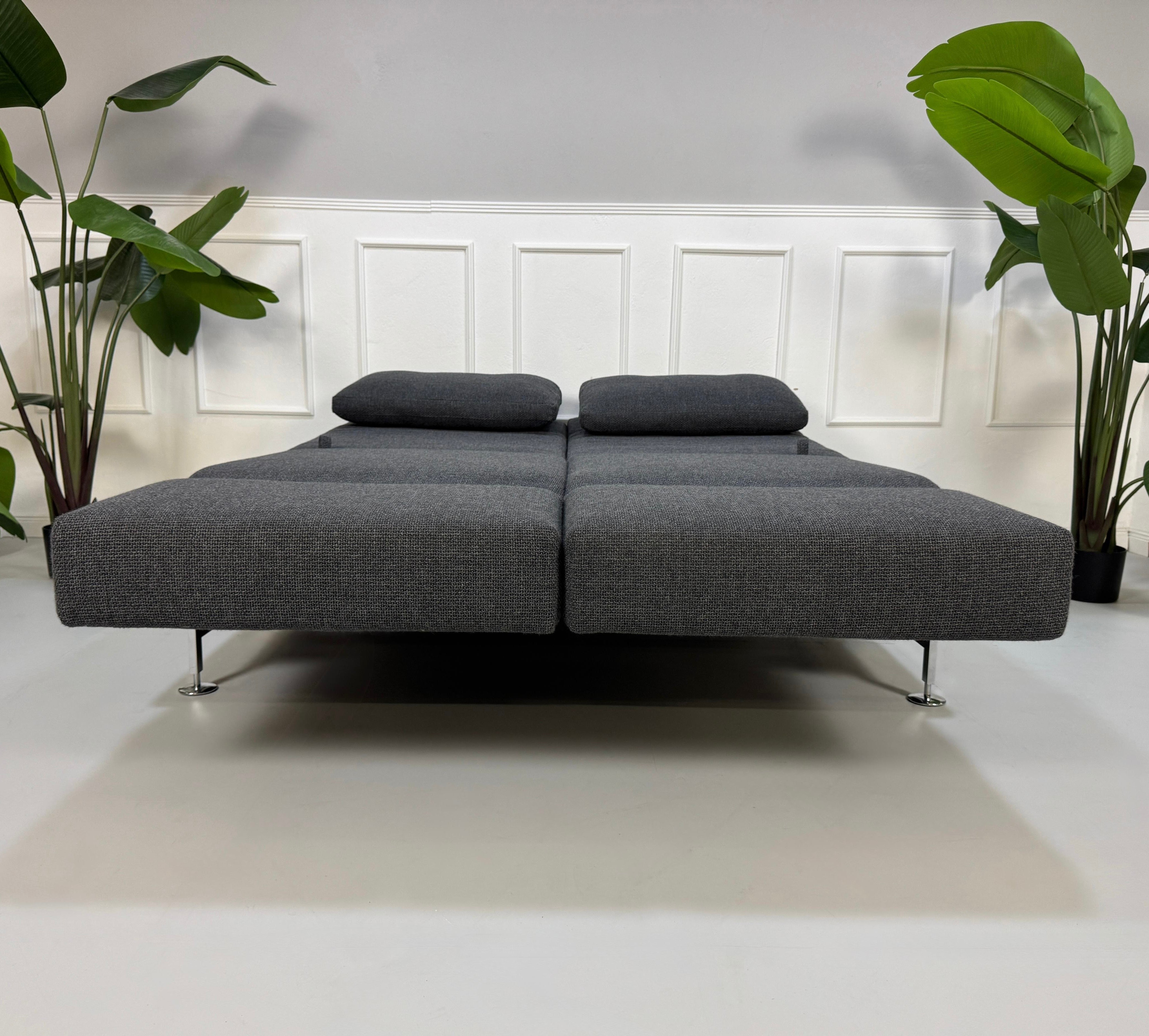 Graues Ausstellungsstück Brühl Moule Designer Stoff Sofa vor einer Wand, stilvoll und modern eingerichtet.