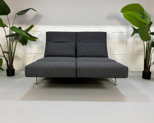 Graues Ausstellungsstück Brühl Moule Designer Stoff Sofa vor einer Wand, stilvoll und modern eingerichtet.