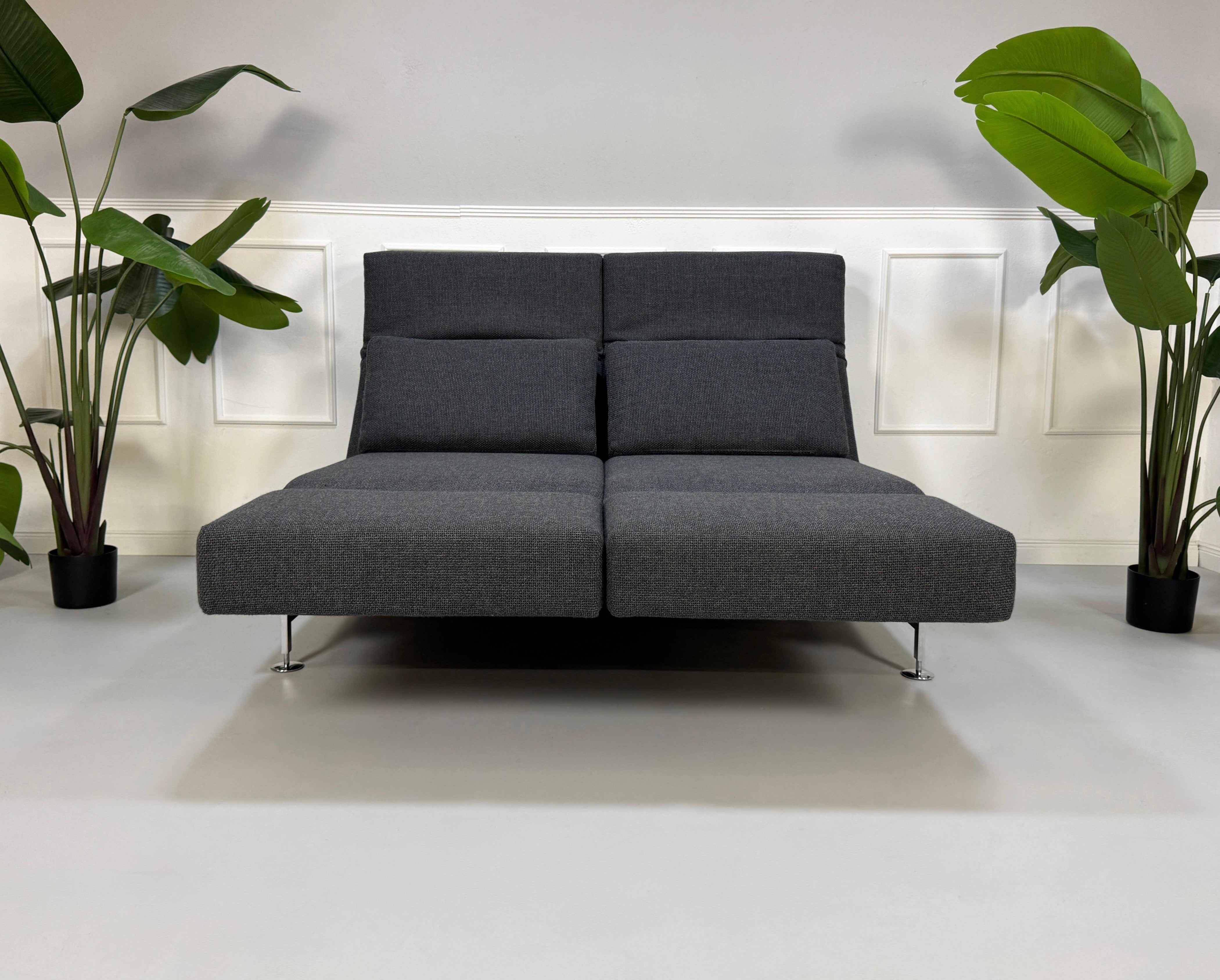 Graues Ausstellungsstück Brühl Moule Designer Stoff Sofa vor einer Wand, stilvoll und modern eingerichtet.