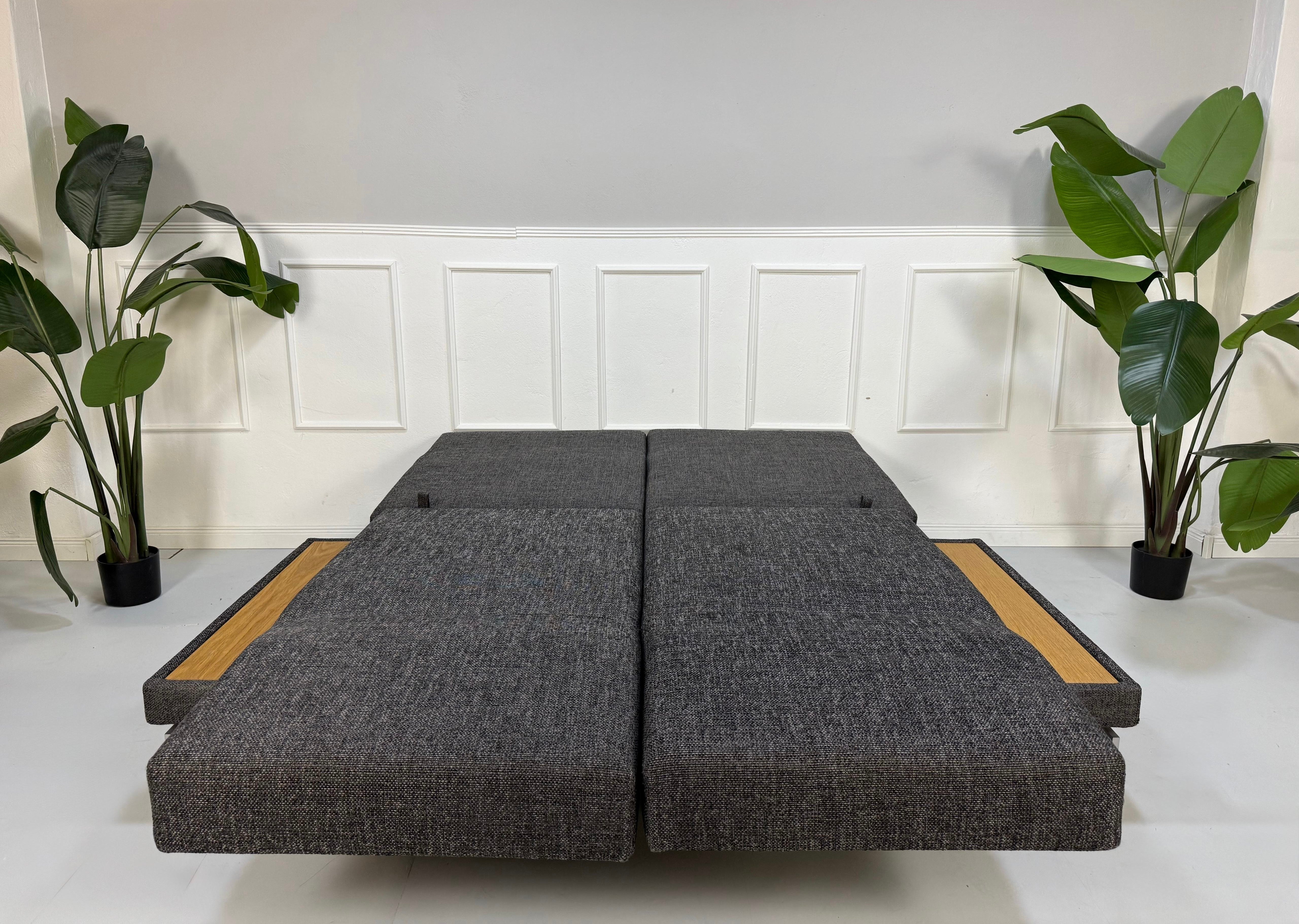 Ausstellungsstück Brühl Moule Designer Stoff Sofa in Grau vor einer Wand, stilvoll und modern eingerichtet.