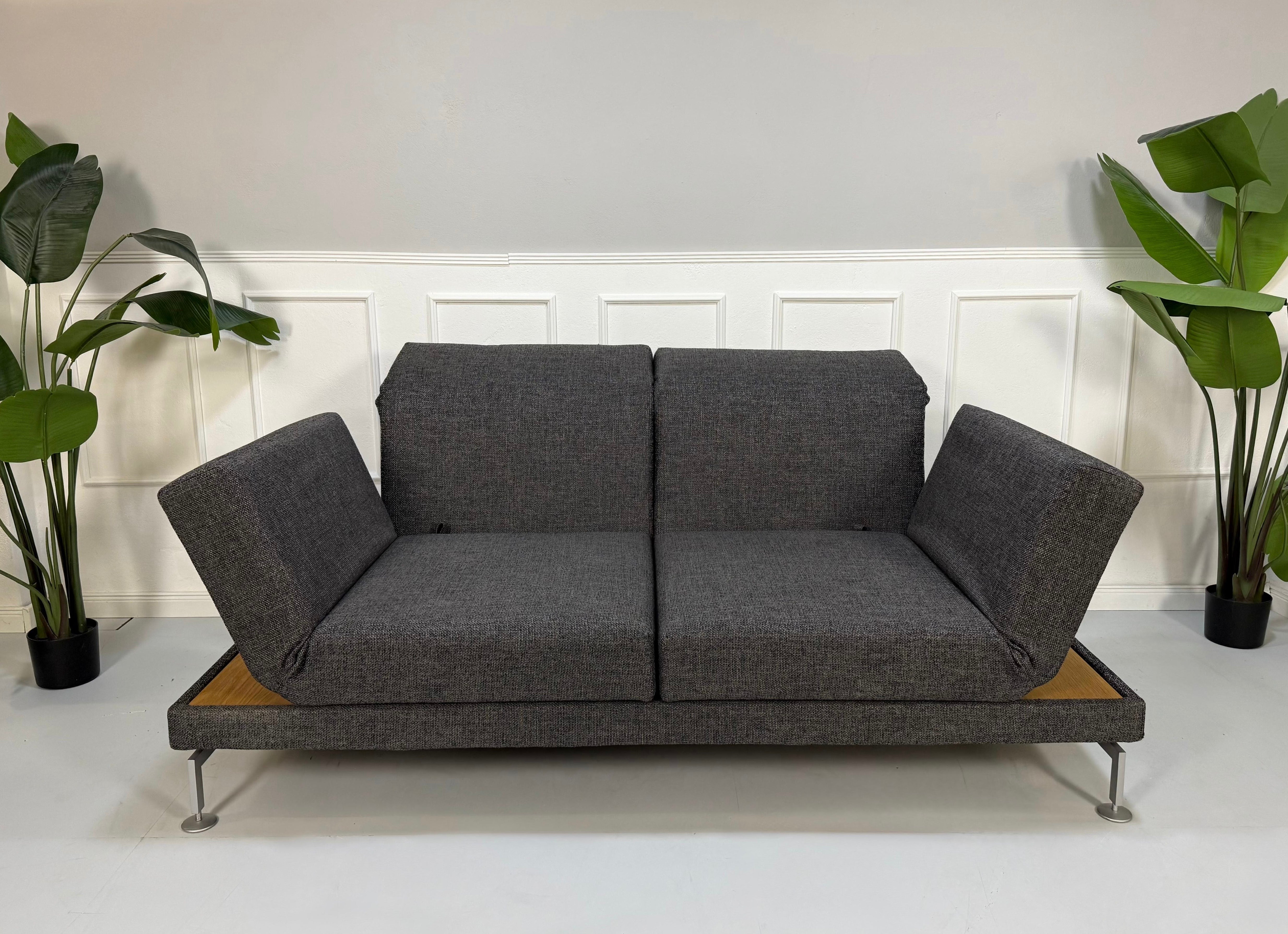 Ausstellungsstück Brühl Moule Designer Stoff Sofa in Grau vor einer Wand, stilvoll und modern eingerichtet.
