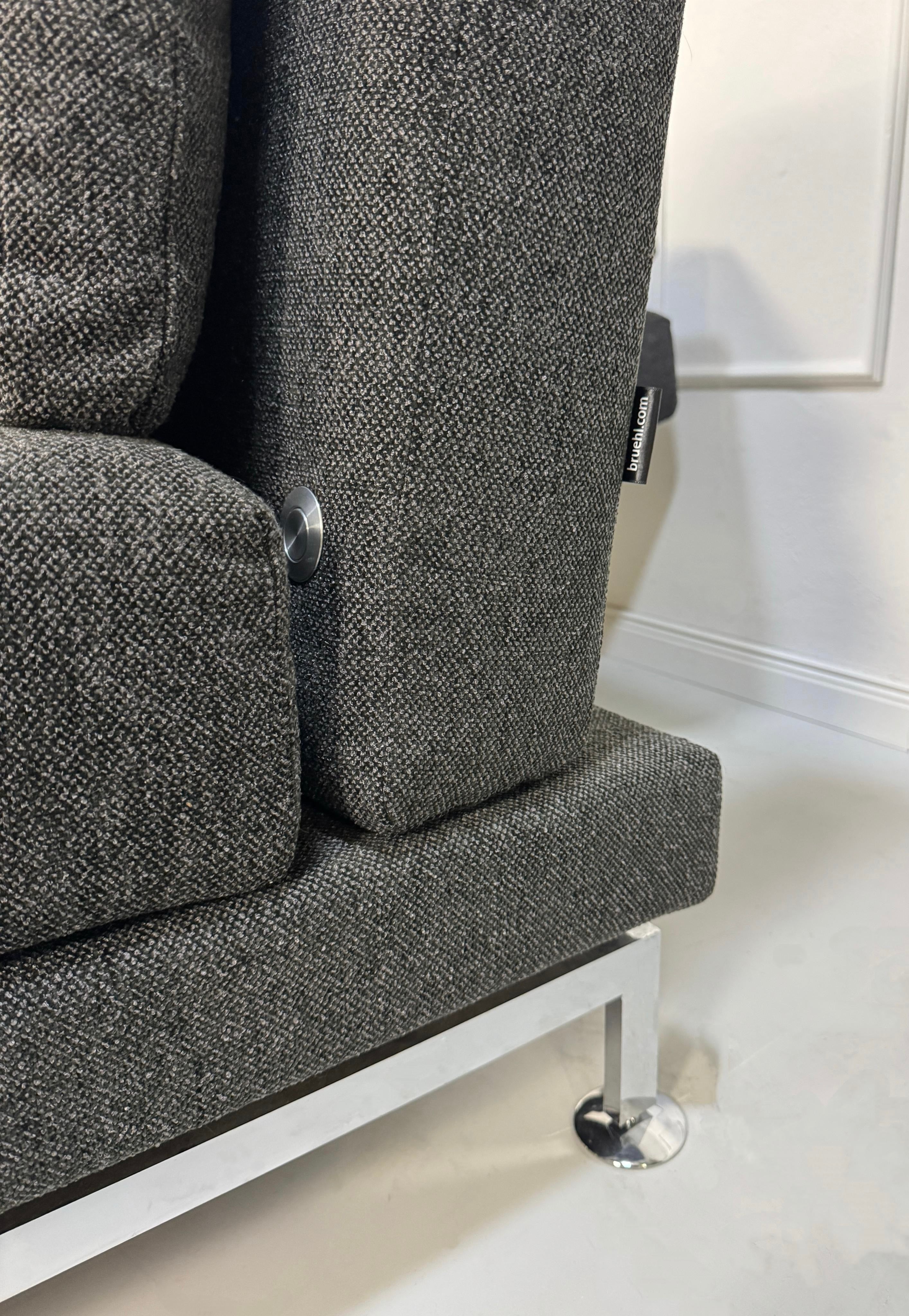 Erneuertes graues Brühl Moule Designer Stoff Sofa vor einer Wand, stilvoll und modern eingerichtet.