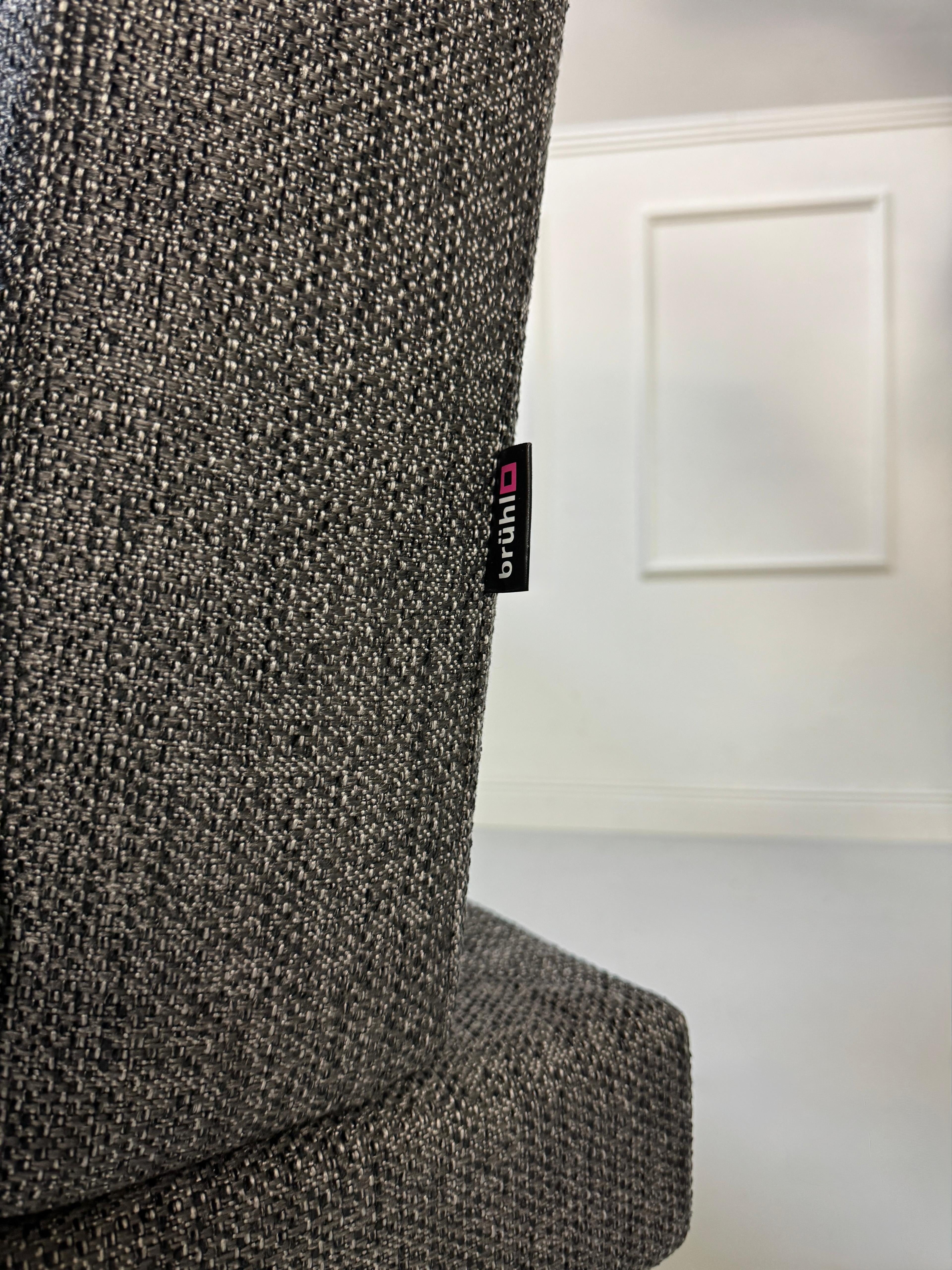 Anthrazit Brühl Moule Small Designer Stoff Sofa vor einer Wand, stilvoll und modern eingerichtet.