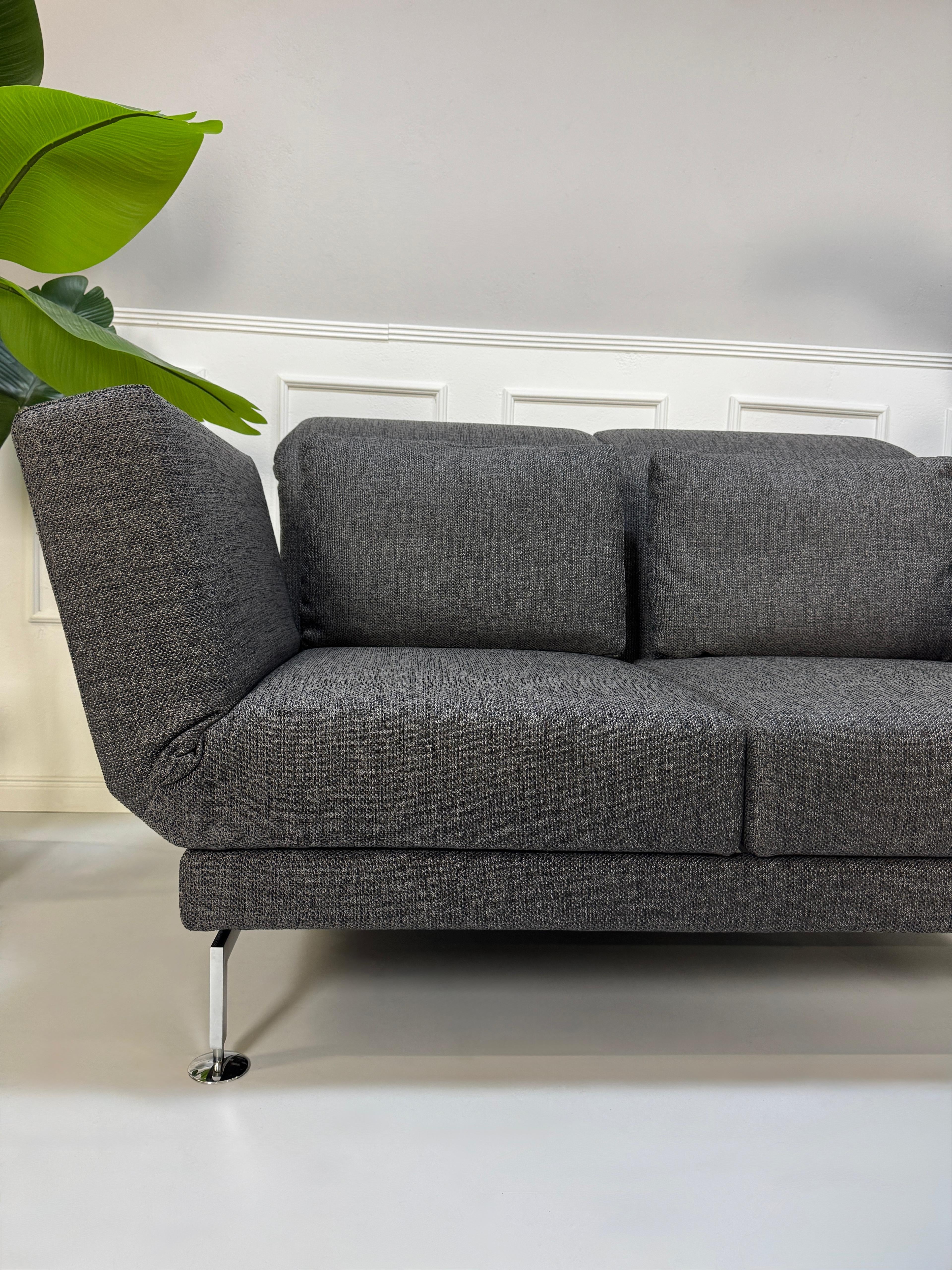 Anthrazit Brühl Moule Small Designer Stoff Sofa vor einer Wand, stilvoll und modern eingerichtet.