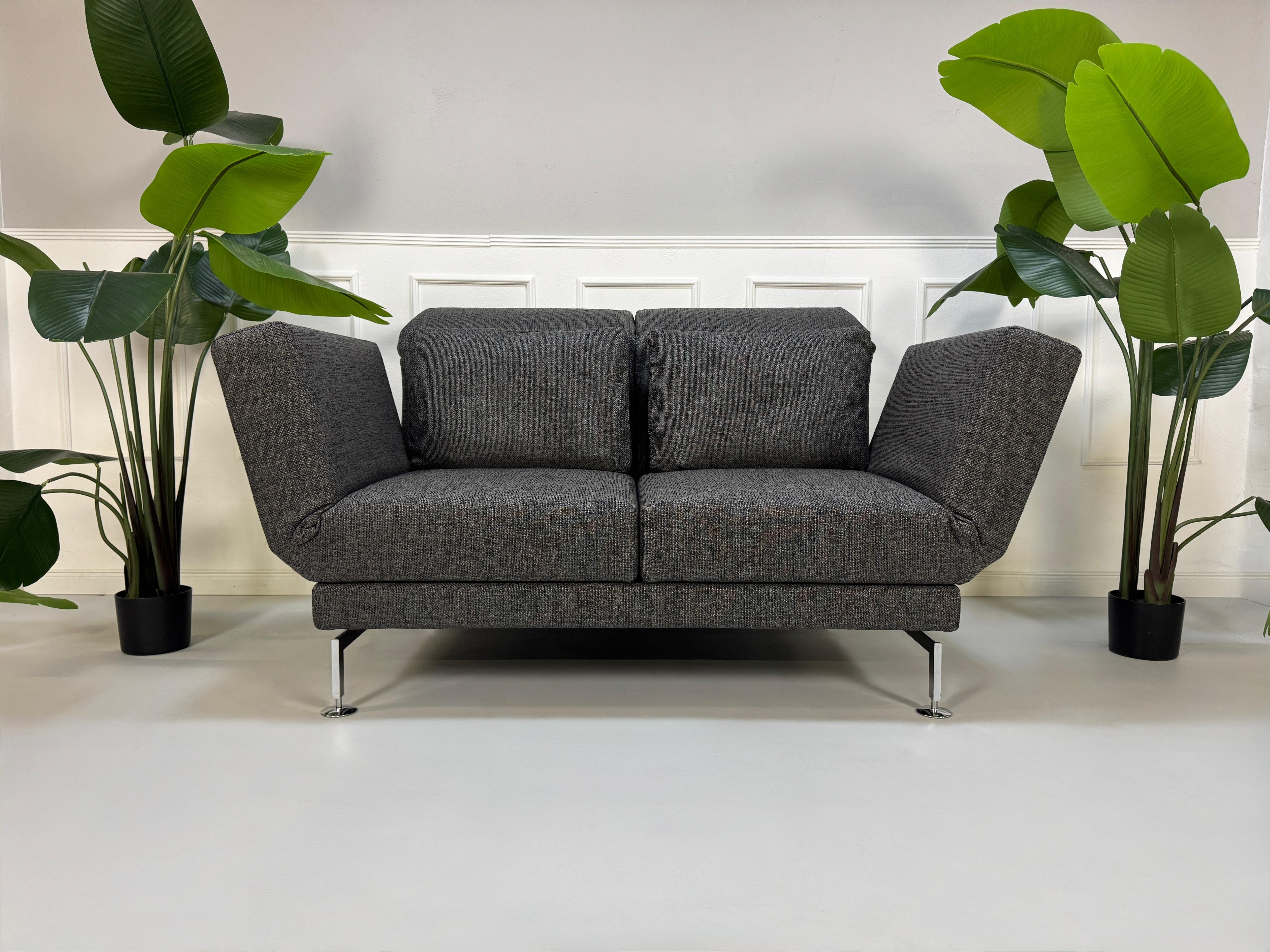 Anthrazit Brühl Moule Small Designer Stoff Sofa vor einer Wand, stilvoll und modern eingerichtet.