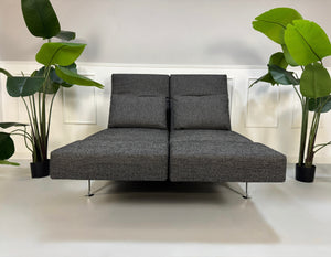 Anthrazit Brühl Moule Small Designer Stoff Sofa vor einer Wand, stilvoll und modern eingerichtet.