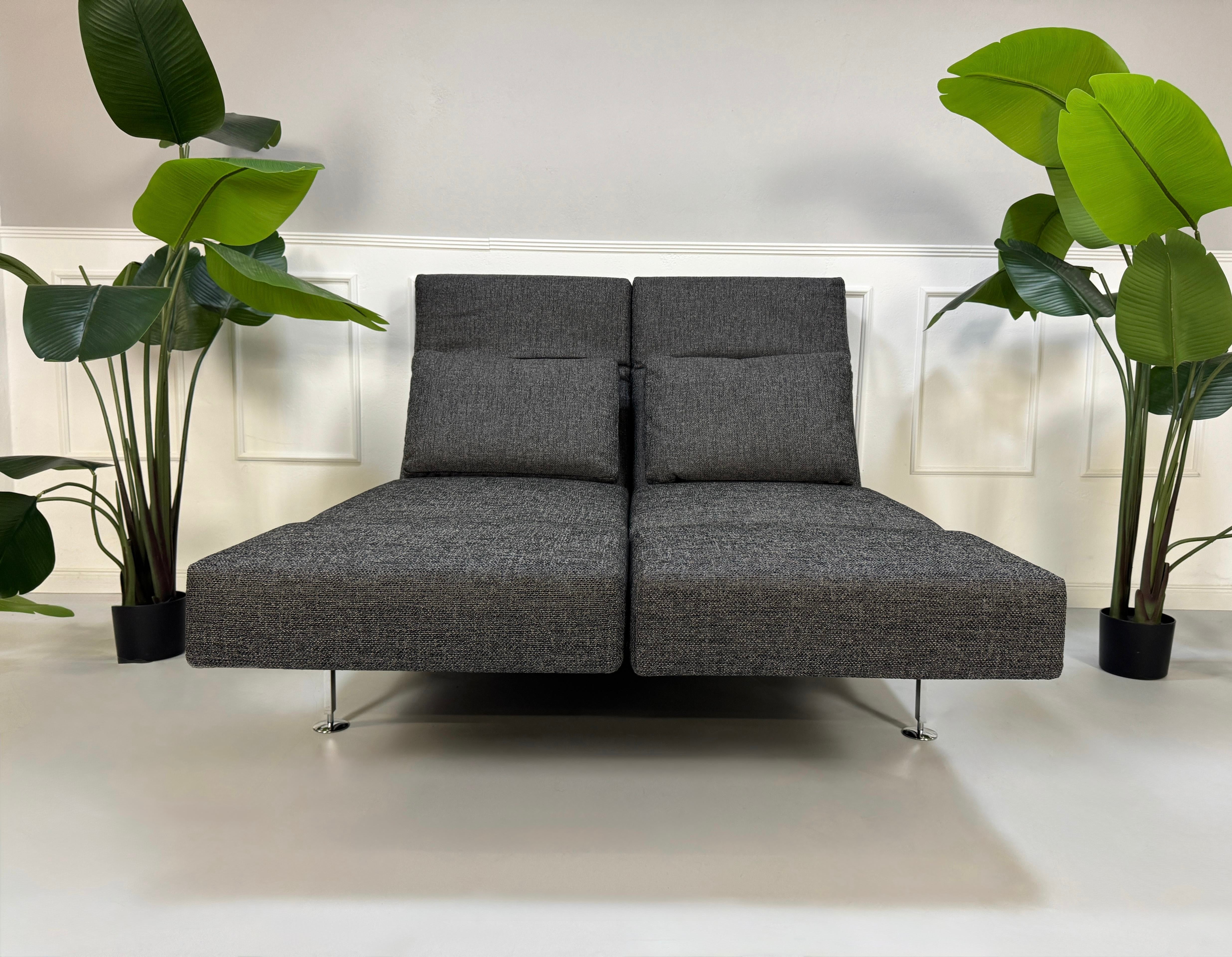 Anthrazit Brühl Moule Small Designer Stoff Sofa vor einer Wand, stilvoll und modern eingerichtet.