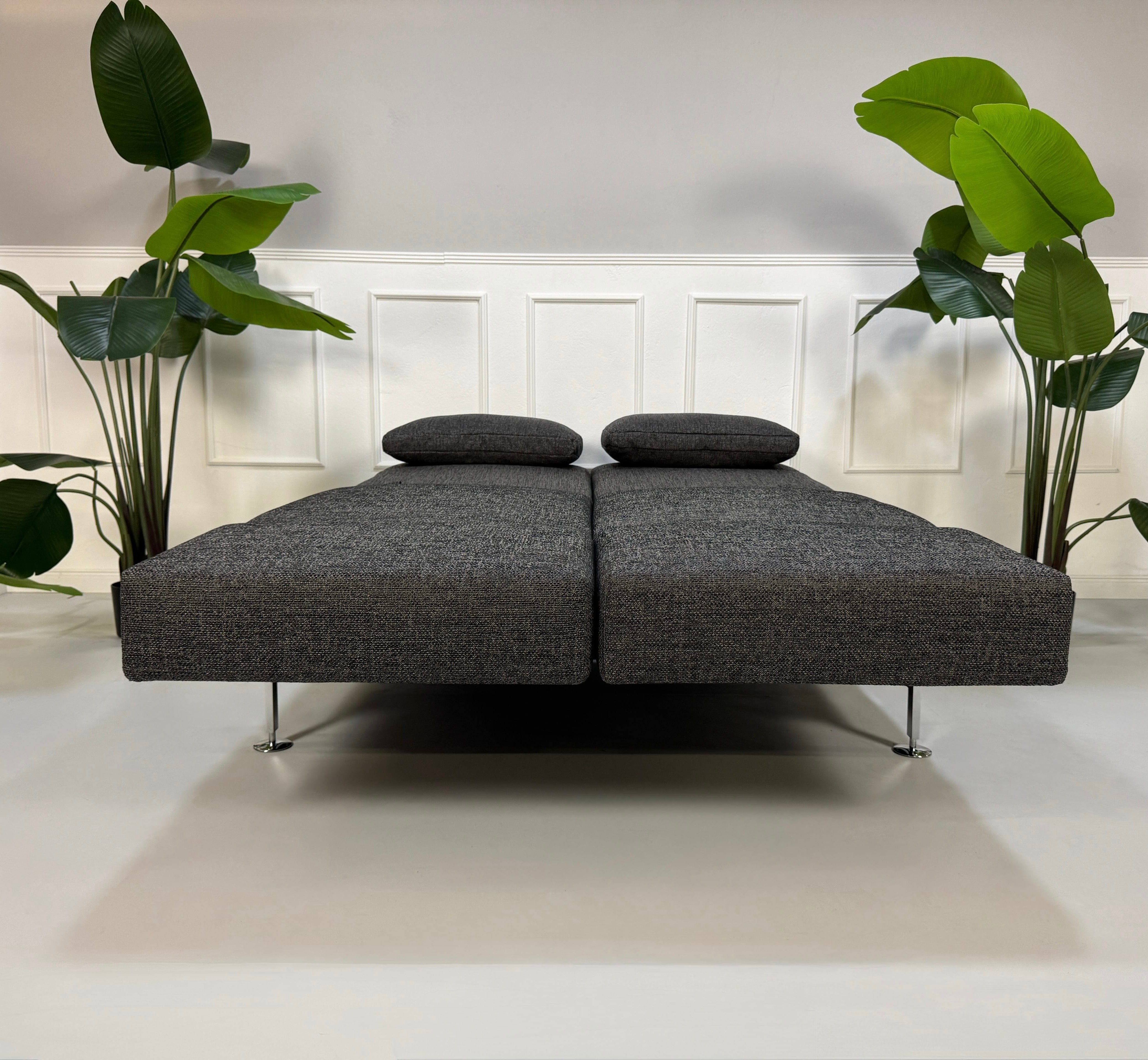 Anthrazit Brühl Moule Small Designer Stoff Sofa vor einer Wand, stilvoll und modern eingerichtet.