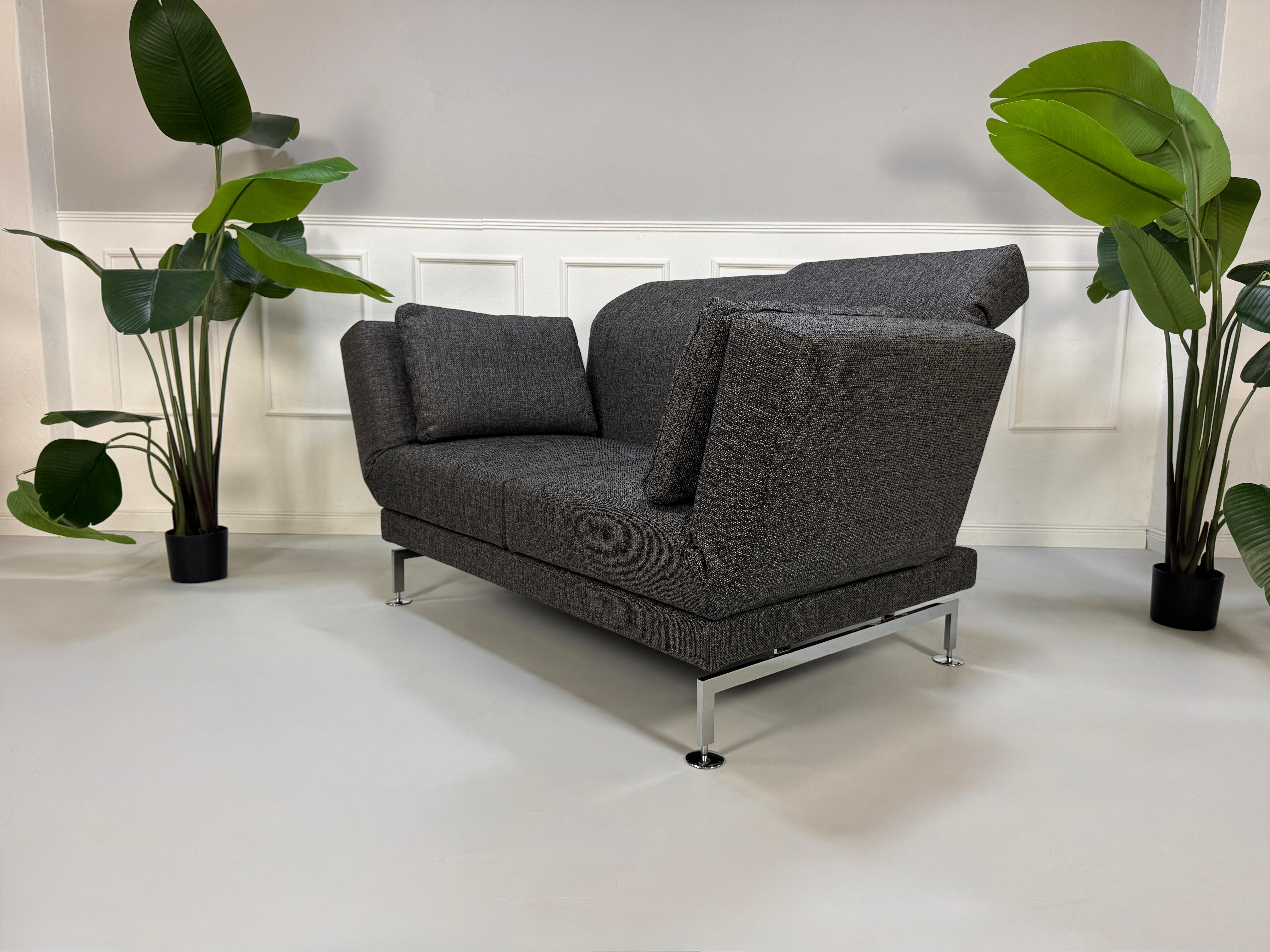 Anthrazit Brühl Moule Small Designer Stoff Sofa vor einer Wand, stilvoll und modern eingerichtet.