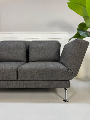 Anthrazit Brühl Moule Small Designer Stoff Sofa vor einer Wand, stilvoll und modern eingerichtet.