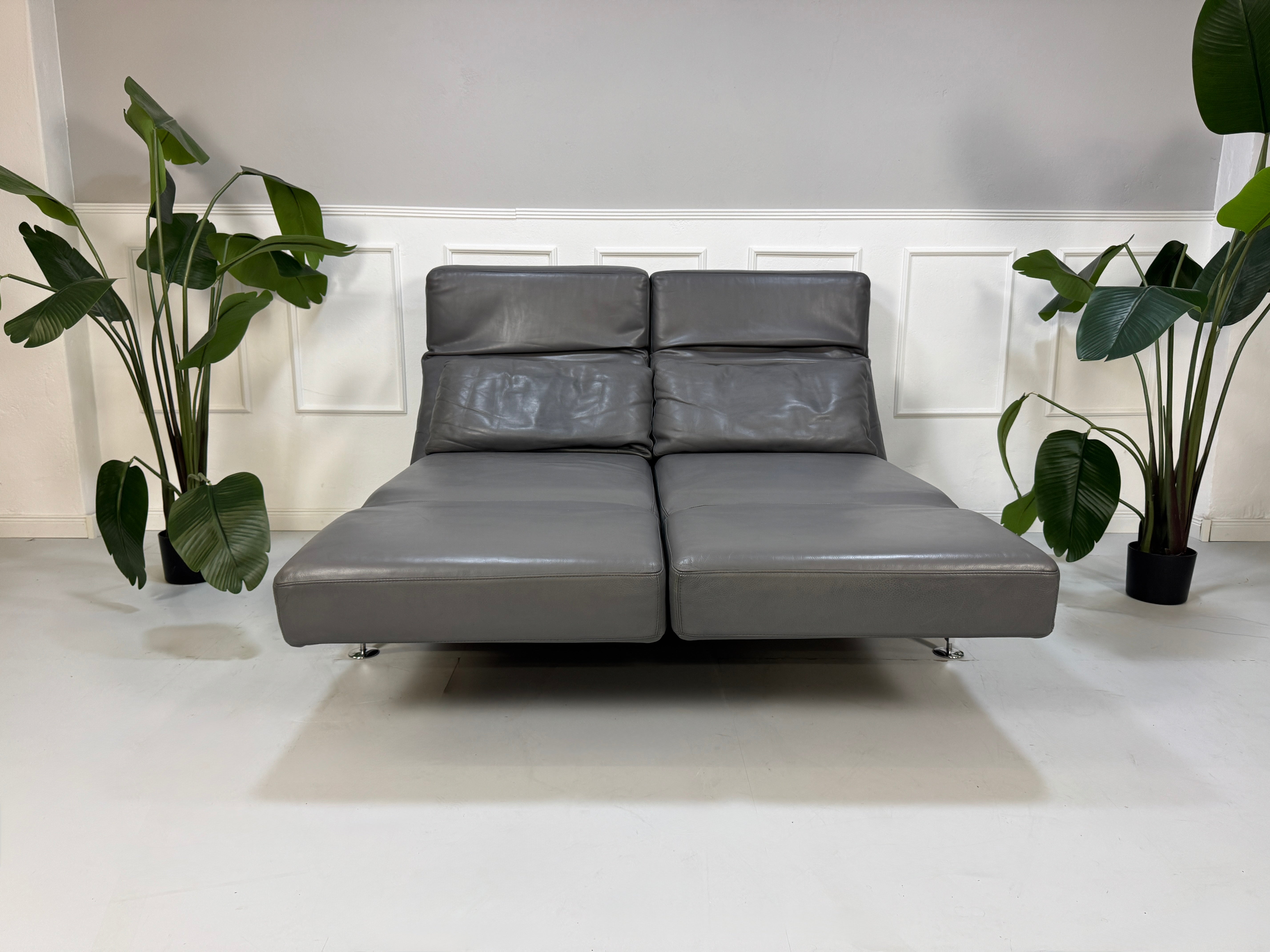Refurbished graues Brühl Moule Designer Leder Sofa vor einer Wand, stilvoll und modern eingerichtet.