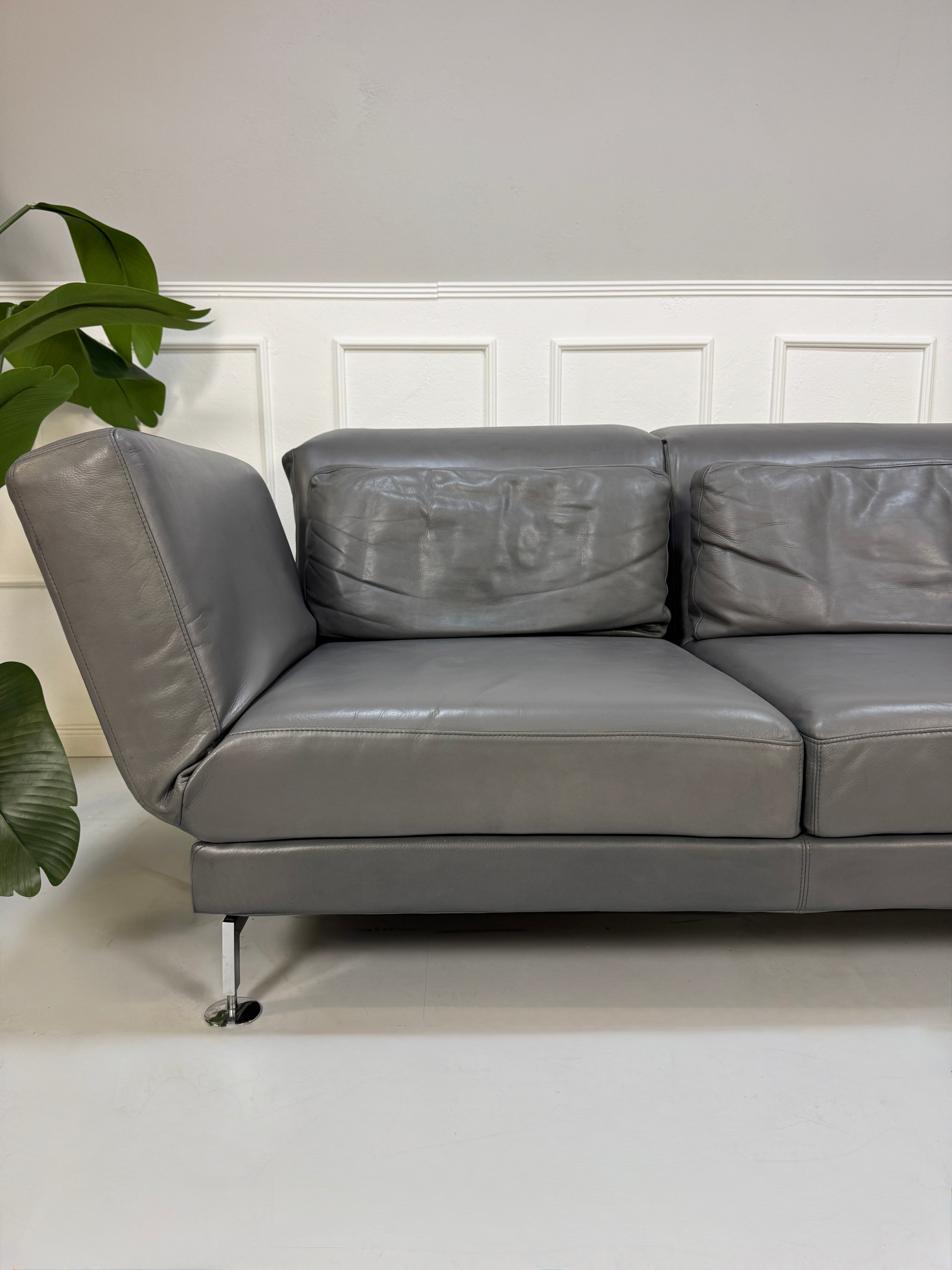 Refurbished graues Brühl Moule Designer Leder Sofa vor einer Wand, stilvoll und modern eingerichtet.