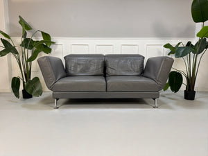 Refurbished graues Brühl Moule Designer Leder Sofa vor einer Wand, stilvoll und modern eingerichtet.