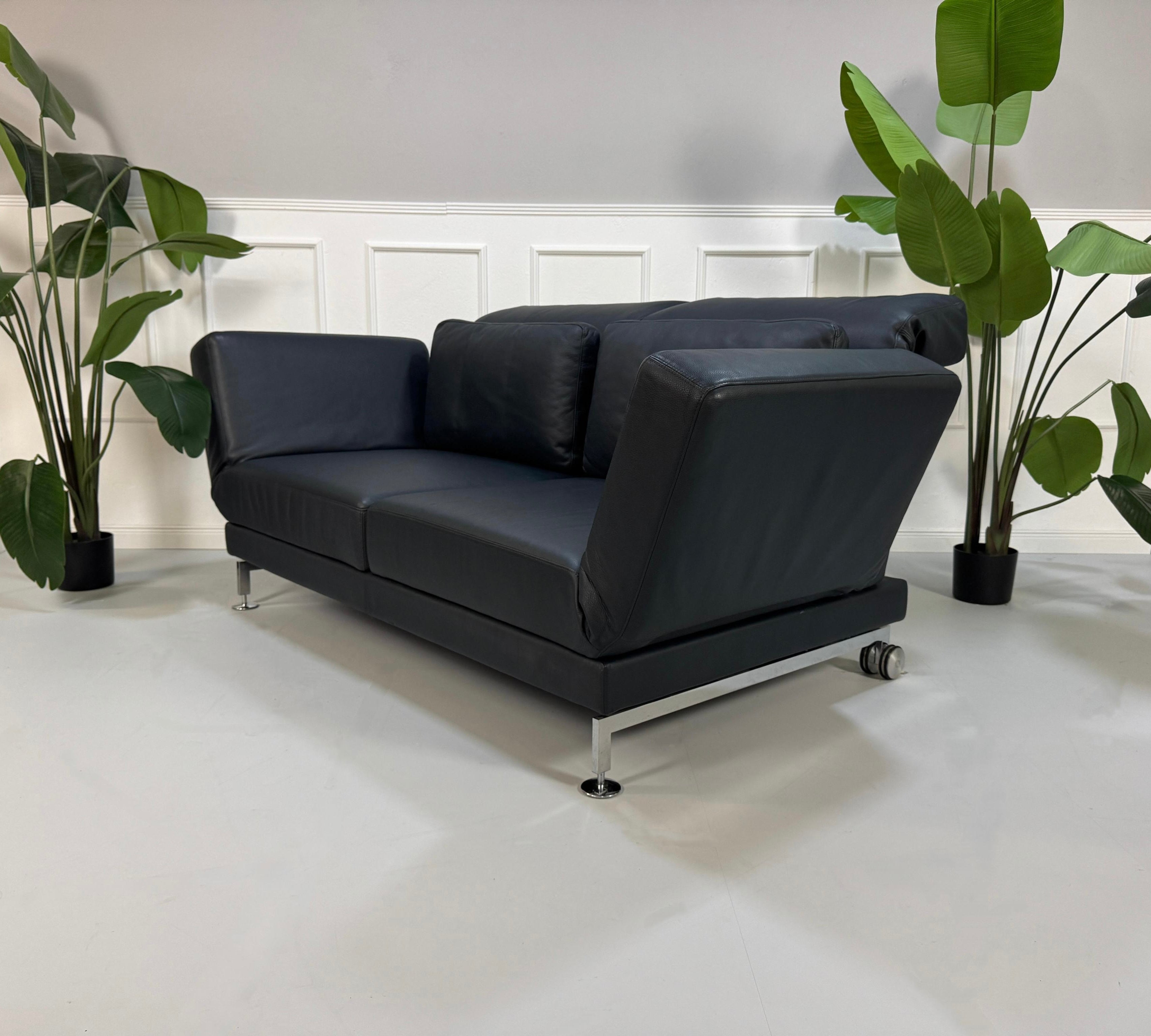 Gebrauchtes blaues Brühl Moule Designer Leder Sofa vor einer Wand, stilvoll und modern eingerichtet.