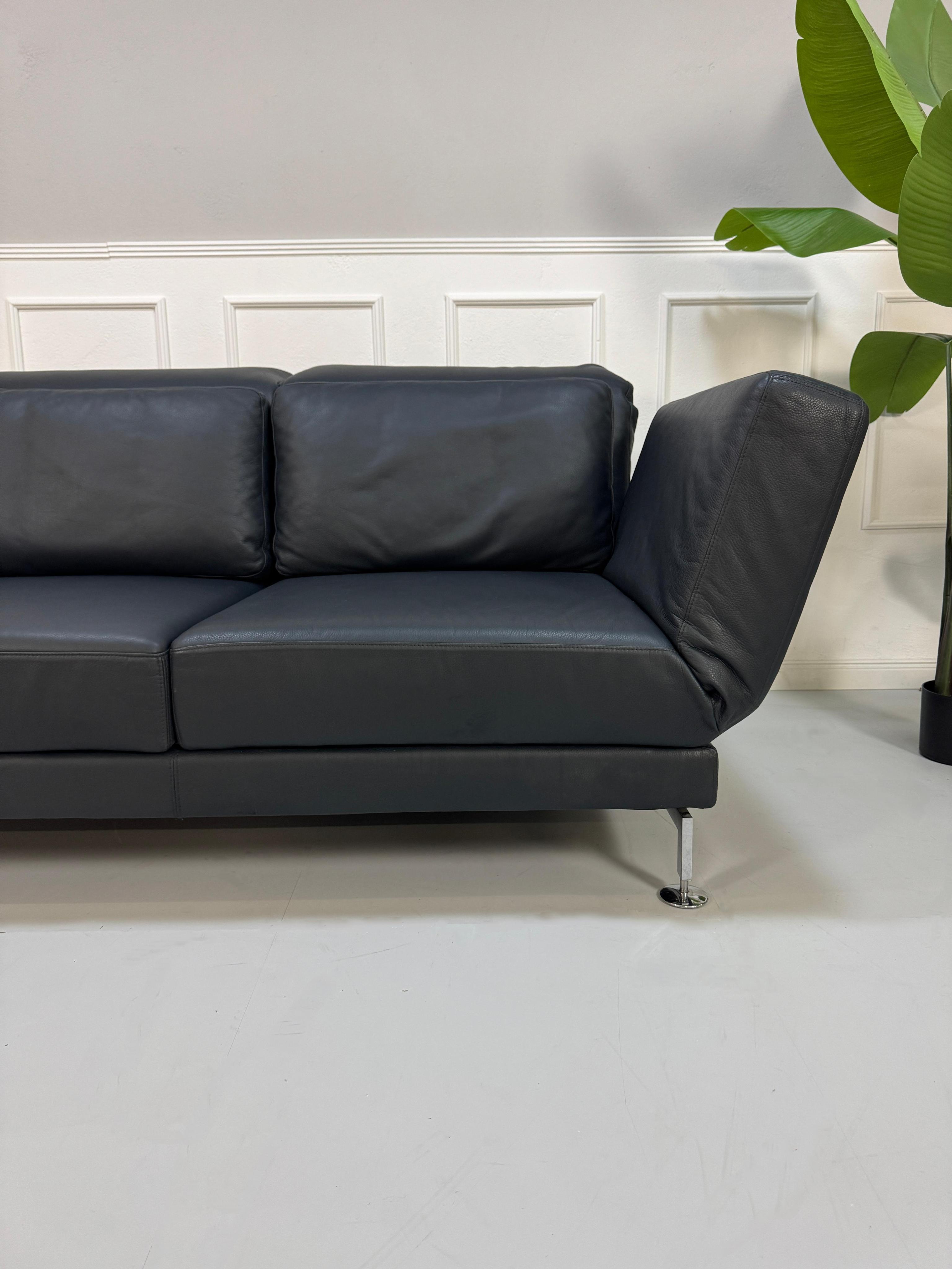 Gebrauchtes blaues Brühl Moule Designer Leder Sofa vor einer Wand, stilvoll und modern eingerichtet.