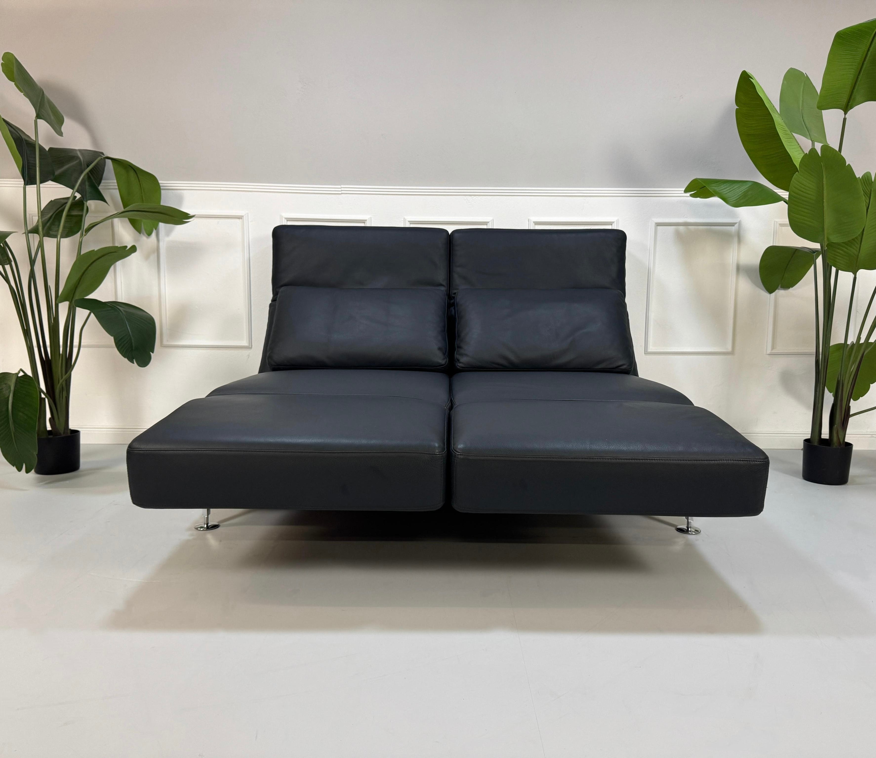 Gebrauchtes blaues Brühl Moule Designer Leder Sofa vor einer Wand, stilvoll und modern eingerichtet.