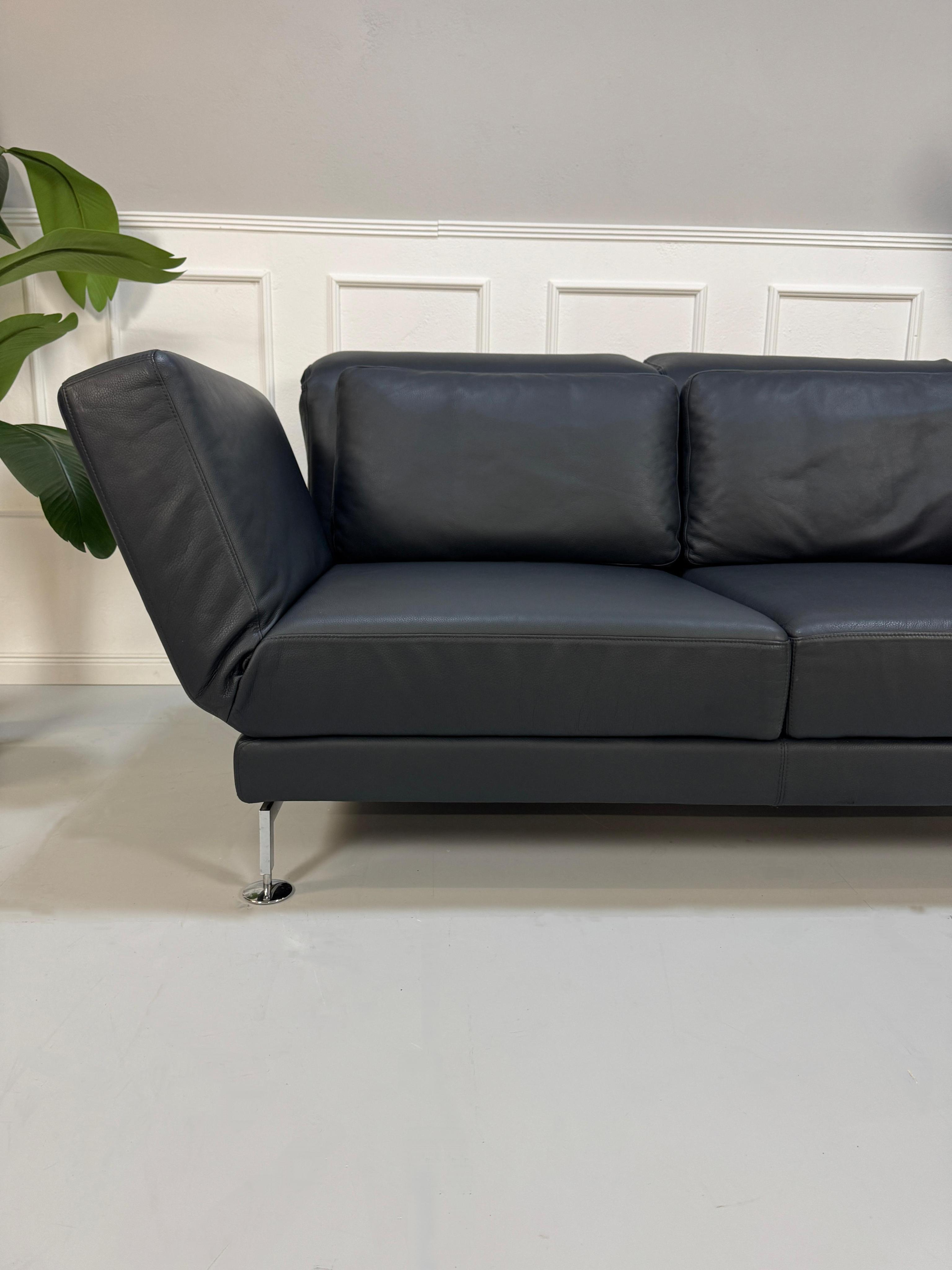 Gebrauchtes blaues Brühl Moule Designer Leder Sofa vor einer Wand, stilvoll und modern eingerichtet.