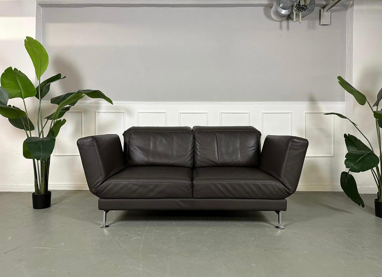 Gebrauchtes Brühl Moule 2-Sitzer Leder Sofa in der Farbe Braun vor einer Wand, stilvoll und modern eingerichtet.