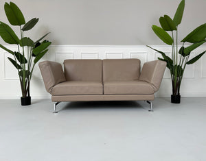 Gebrauchtes Brühl Moule 2-Sitzer Leder Sofa in der Farbe Schlamm vor einer Wand, stilvoll und modern eingerichtet.