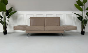 Gebrauchtes Brühl Moule 2-Sitzer Leder Sofa in der Farbe Schlamm vor einer Wand, stilvoll und modern eingerichtet.