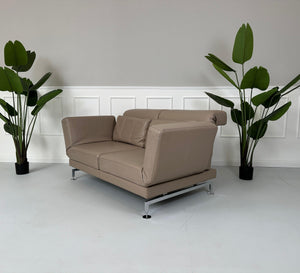 Gebrauchtes Brühl Moule 2-Sitzer Leder Sofa in der Farbe Schlamm vor einer Wand, stilvoll und modern eingerichtet.