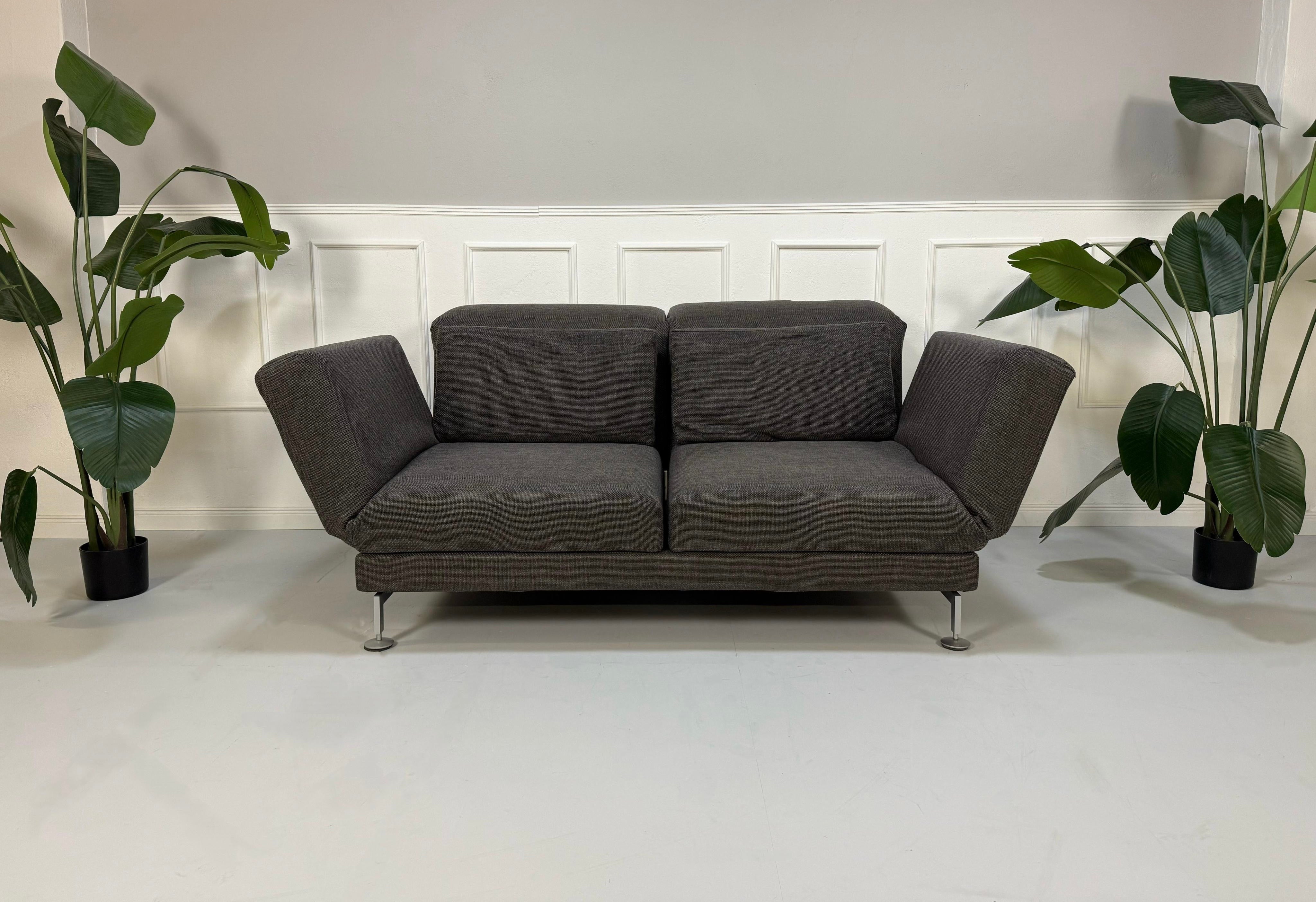 Gebrauchtes graues Brühl Moule Designer Stoff Sofa vor einer Wand, stilvoll und modern eingerichtet.