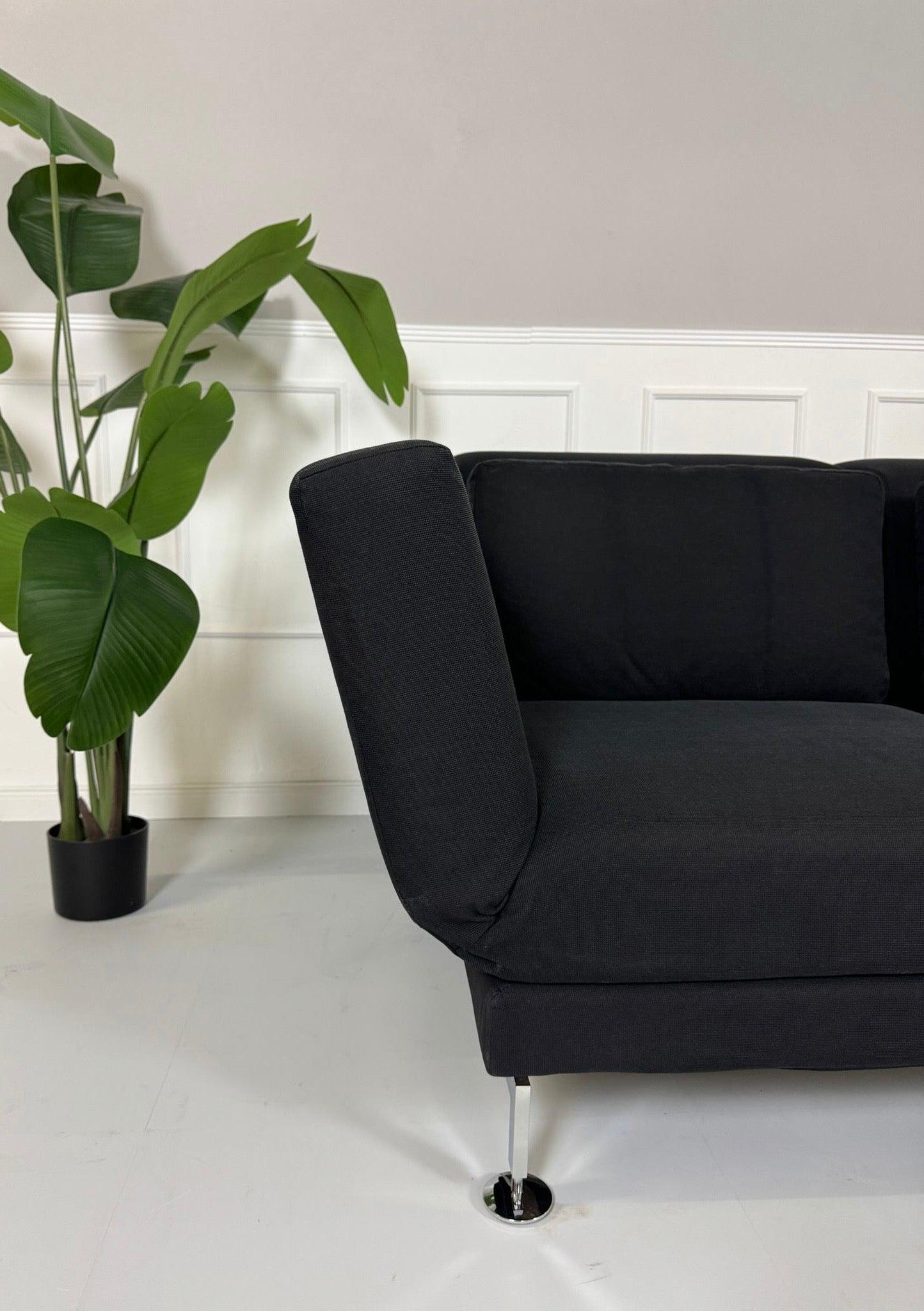 Gebrauchtes Brühl Moule 2-Sitzer Stoff Sofa in der Farbe Schwarz vor einer Wand, stilvoll und modern eingerichtet.