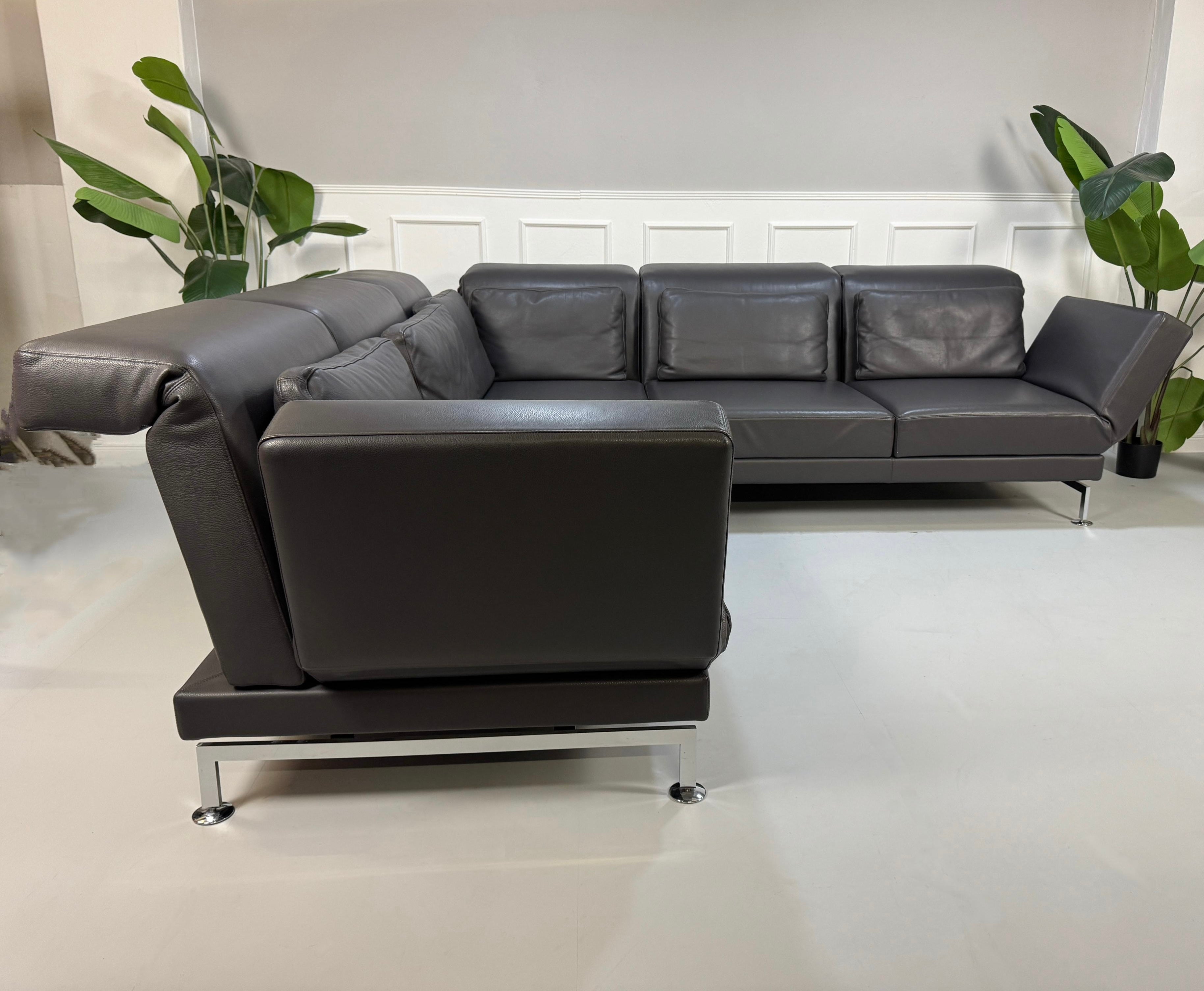 Gebrauchtes graues Brühl Moule Designer Leder Sofa vor einer Wand, stilvoll und modern eingerichtet.