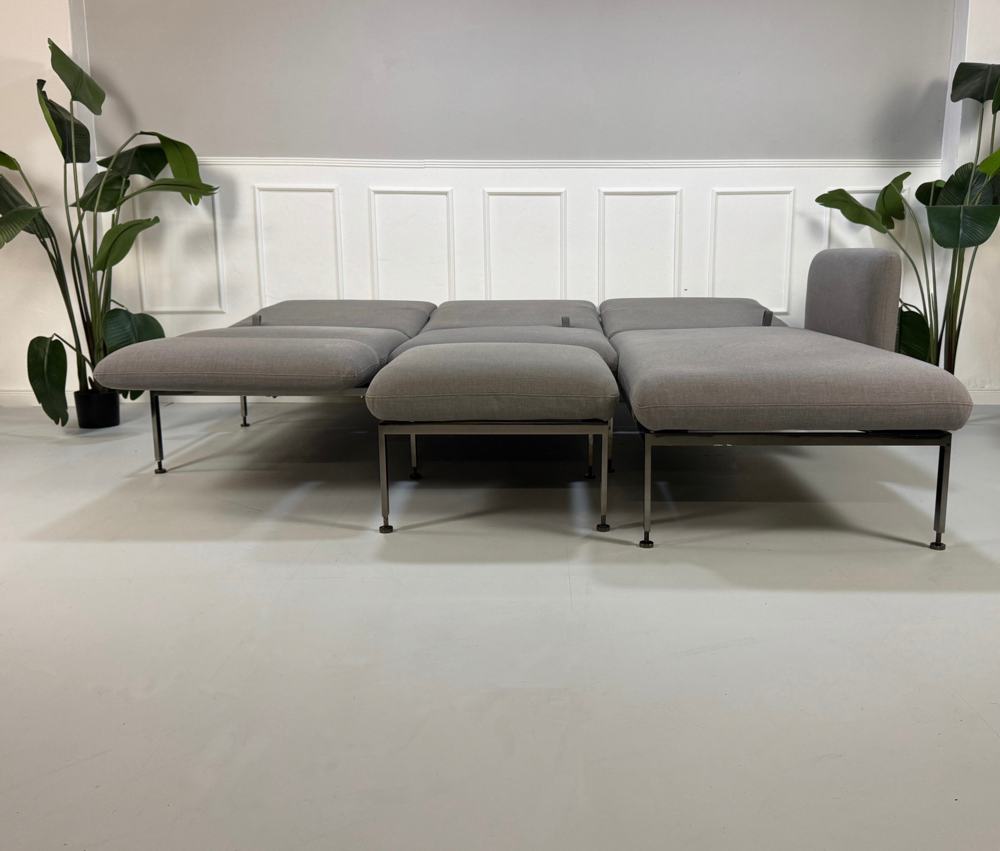 Gebrauchtes graues Brühl Roro Designer Stoff Sofa mit Hocker vor einer Wand, stilvoll und modern eingerichtet.