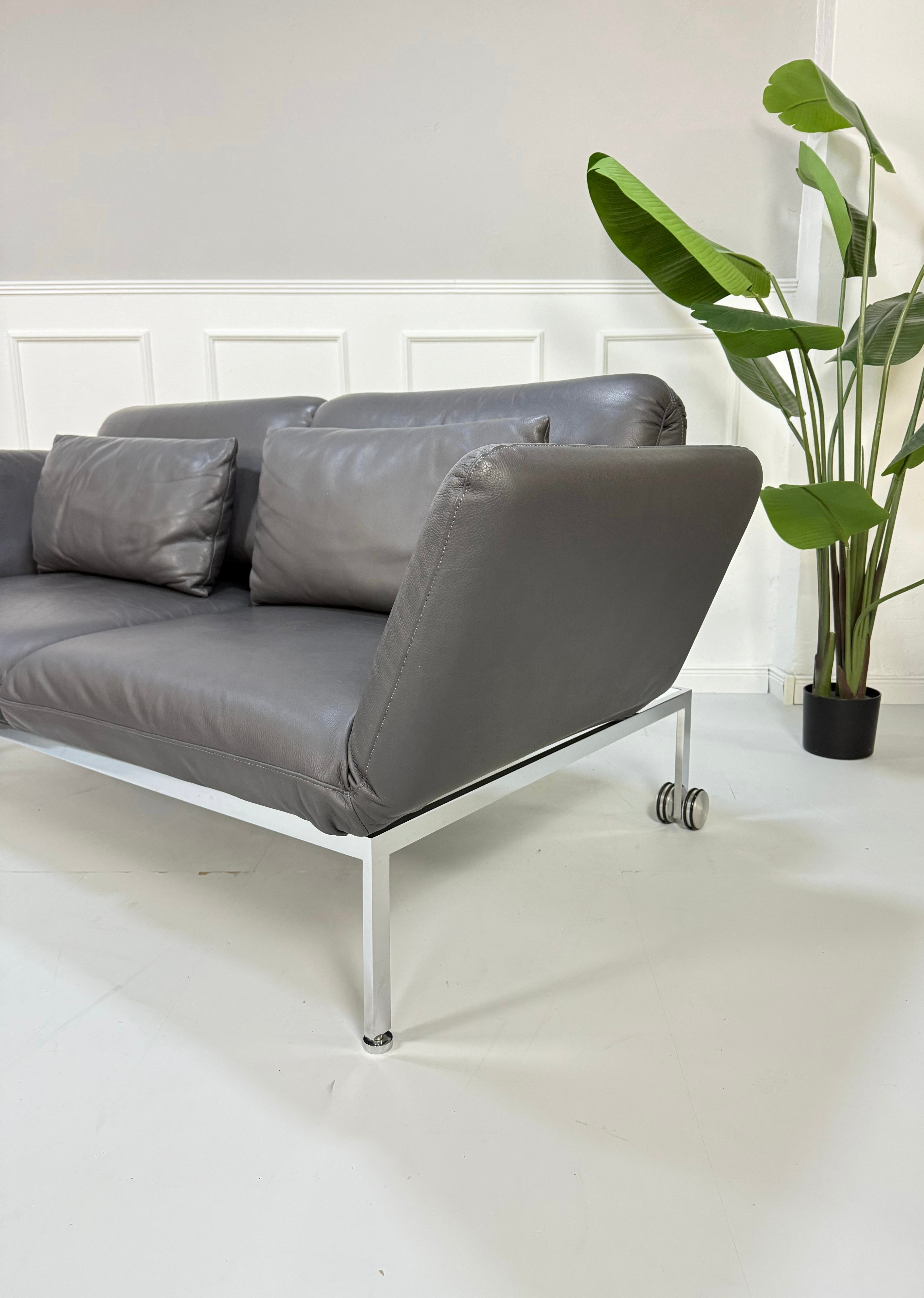 Gebrauchtes graues Brühl Roro Designer Leder Sofa mit Liege vor einer Wand, stilvoll und modern eingerichtet.