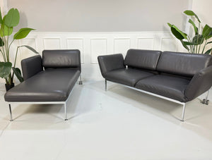 Gebrauchtes graues Brühl Roro Designer Leder Sofa mit Liege vor einer Wand, stilvoll und modern eingerichtet.