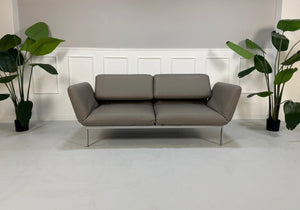 Gebrauchtes graues Brühl Roro Designer Leder Sofa vor einer Wand, stilvoll und modern eingerichtet.
