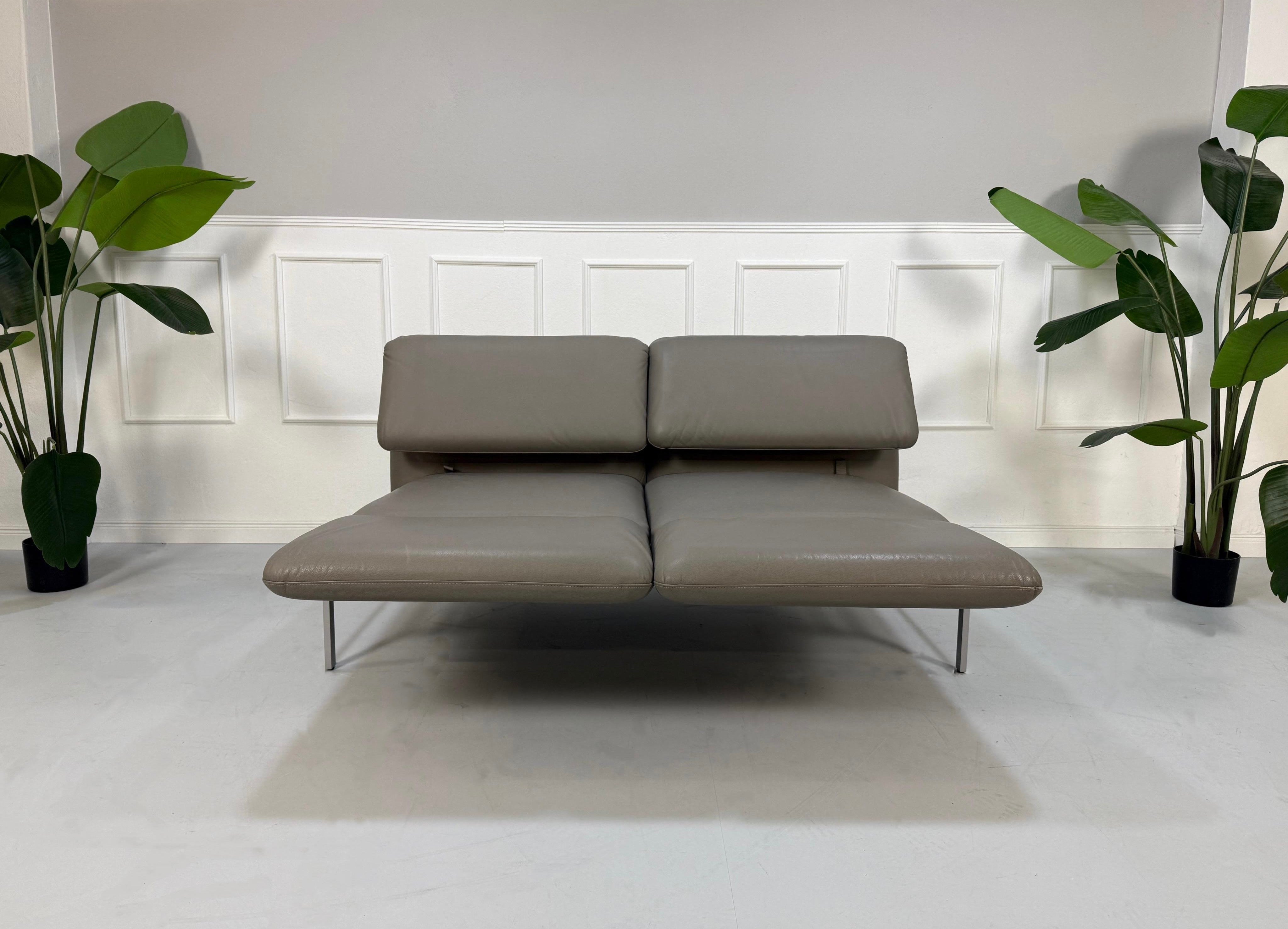Gebrauchtes graues Brühl Roro Designer Leder Sofa vor einer Wand, stilvoll und modern eingerichtet.