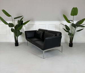 Gebrauchtes schwarzes Brühl Roro Designer Leder Sofa vor einer Wand, stilvoll und modern eingerichtet.