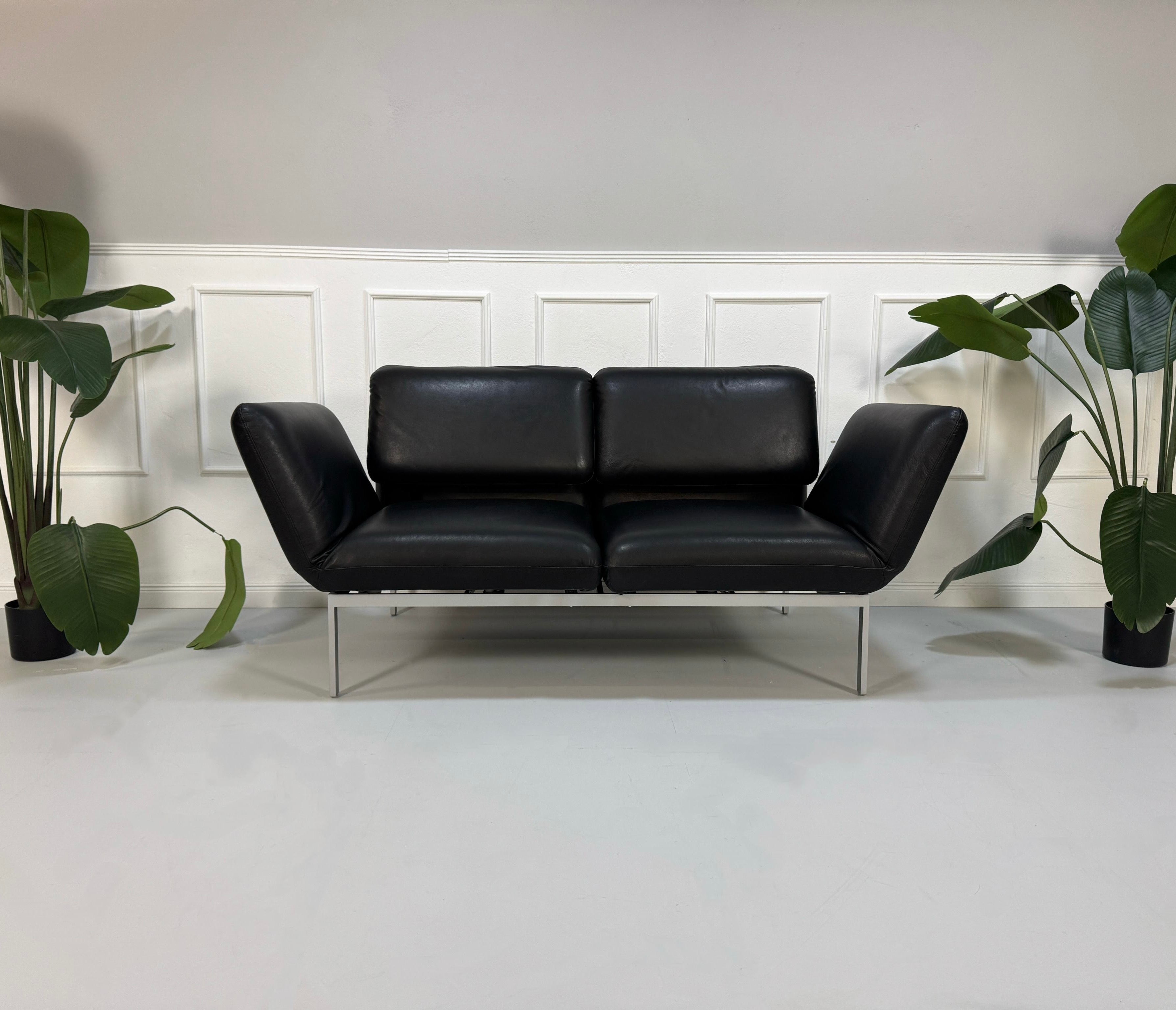 Gebrauchtes schwarzes Brühl Roro Small Designer Leder Sofa vor einer Wand, stilvoll und modern eingerichtet.