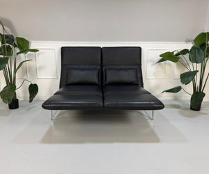 Ausstellungsstück schwarzes Brühl Roro Designer Leder Sofa vor einer Wand, stilvoll und modern eingerichtet.