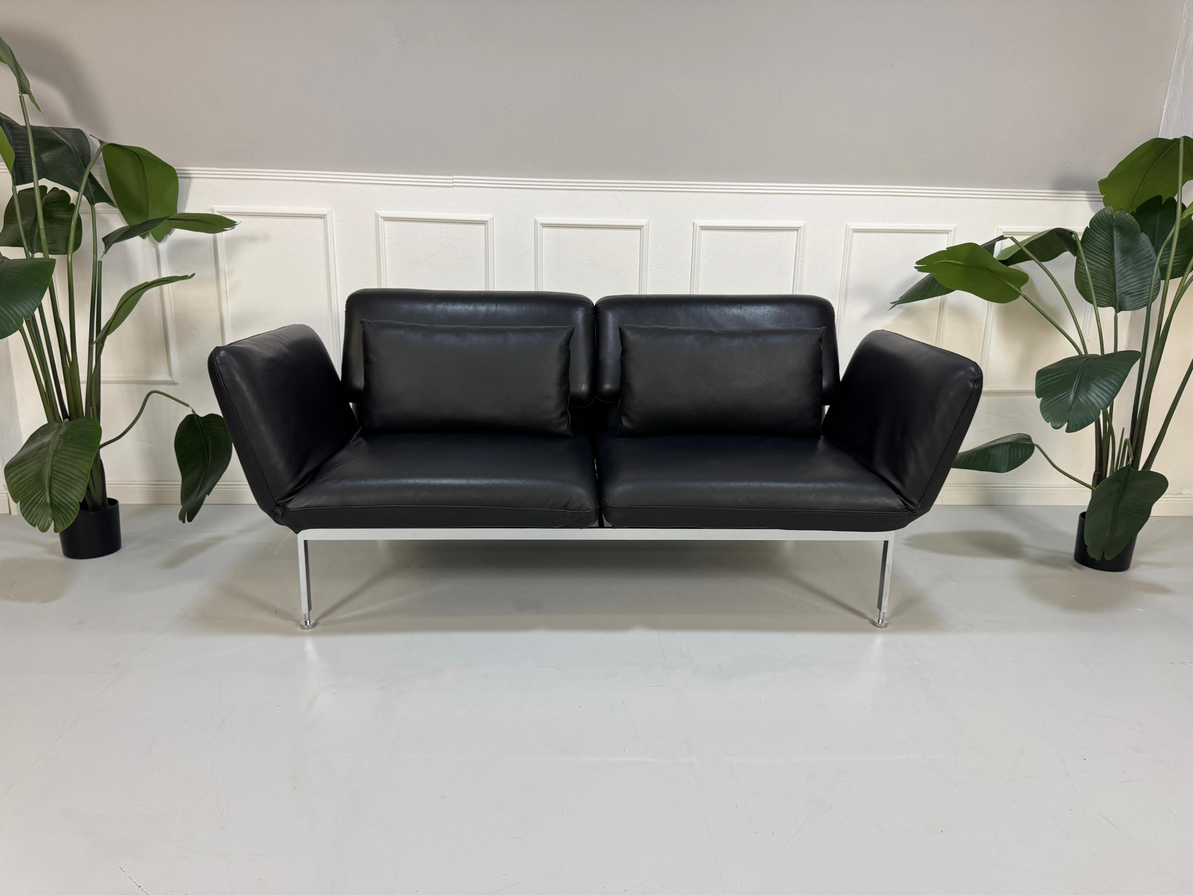 Ausstellungsstück schwarzes Brühl Roro Designer Leder Sofa vor einer Wand, stilvoll und modern eingerichtet.