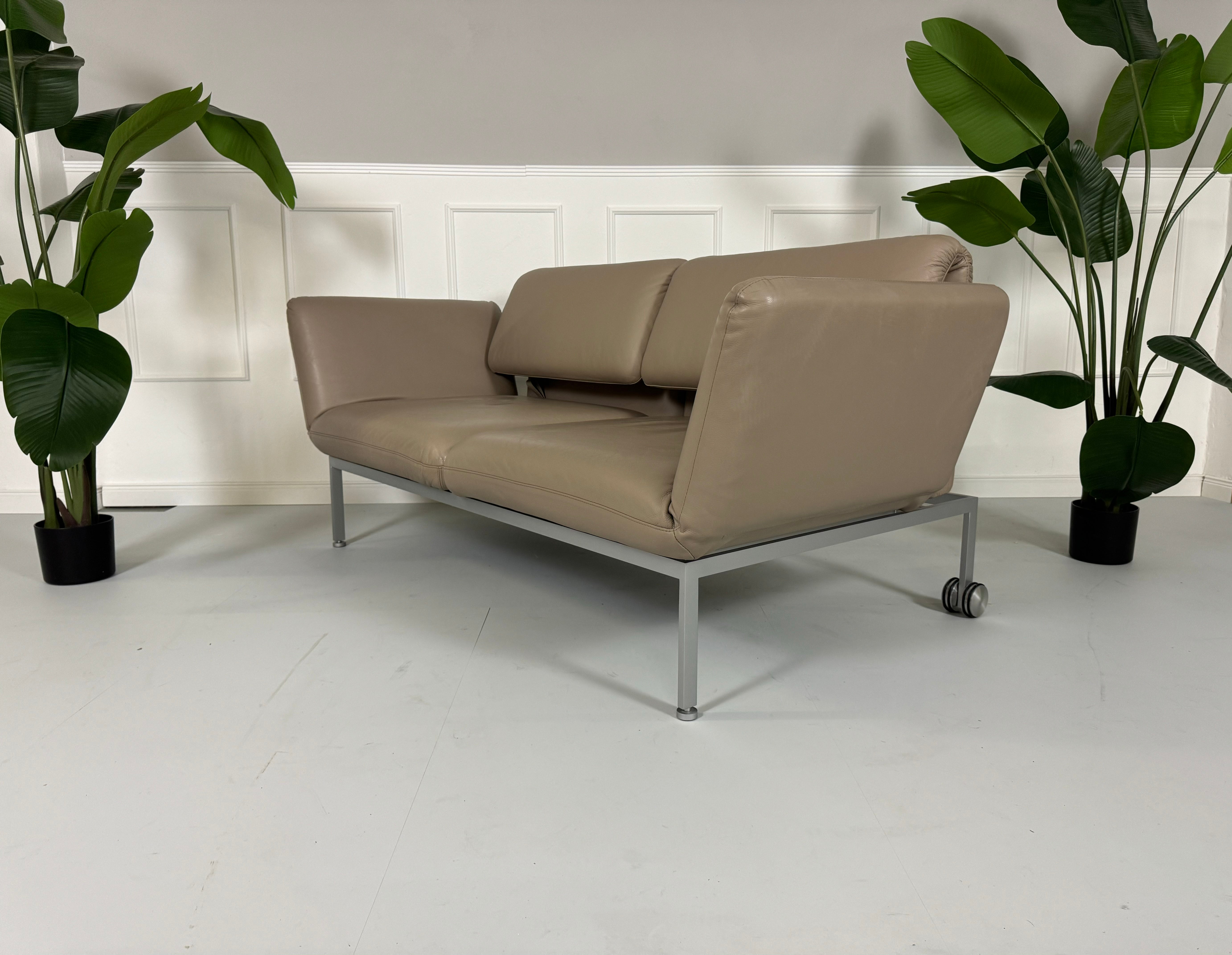 Gebrauchtes Brühl Roro Leder Sofa in der Farbe Schlamm vor einer Wand, stilvoll und modern eingerichtet.