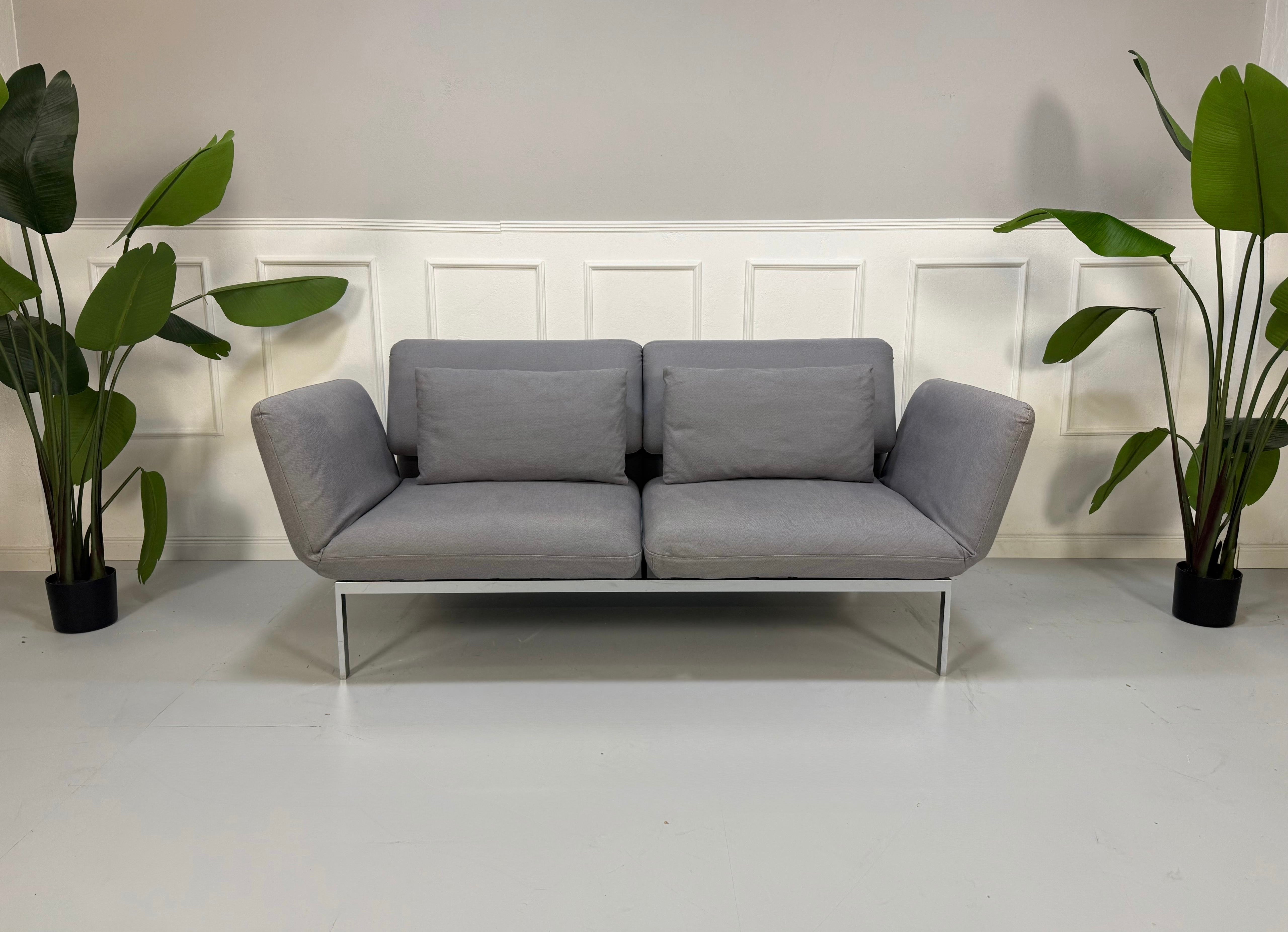 Erneuertes Brühl Roro Designer Stoff Sofa in der Farbe Grau vor einer Wand, stilvoll und modern eingerichtet.