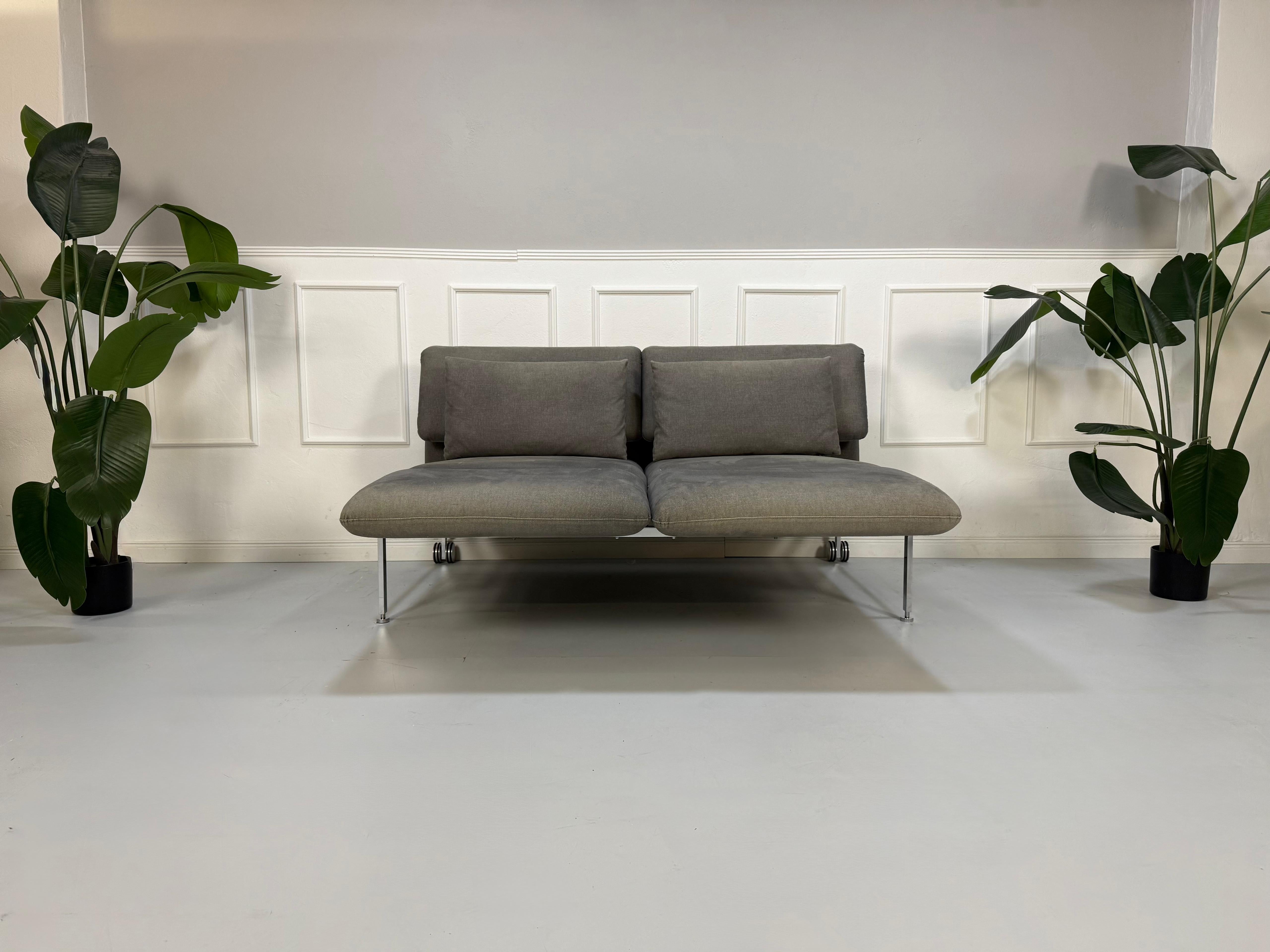 Gebrauchtes graues Brühl Roro Designer Stoff Sofa vor einer Wand, stilvoll und modern eingerichtet.