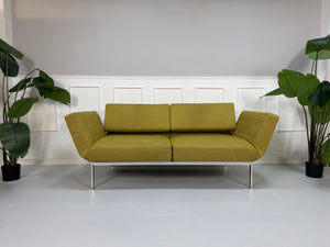 Gebrauchtes grünes Brühl Roro Soft Designer Stoff Sofa vor einer Wand, stilvoll und modern eingerichtet.