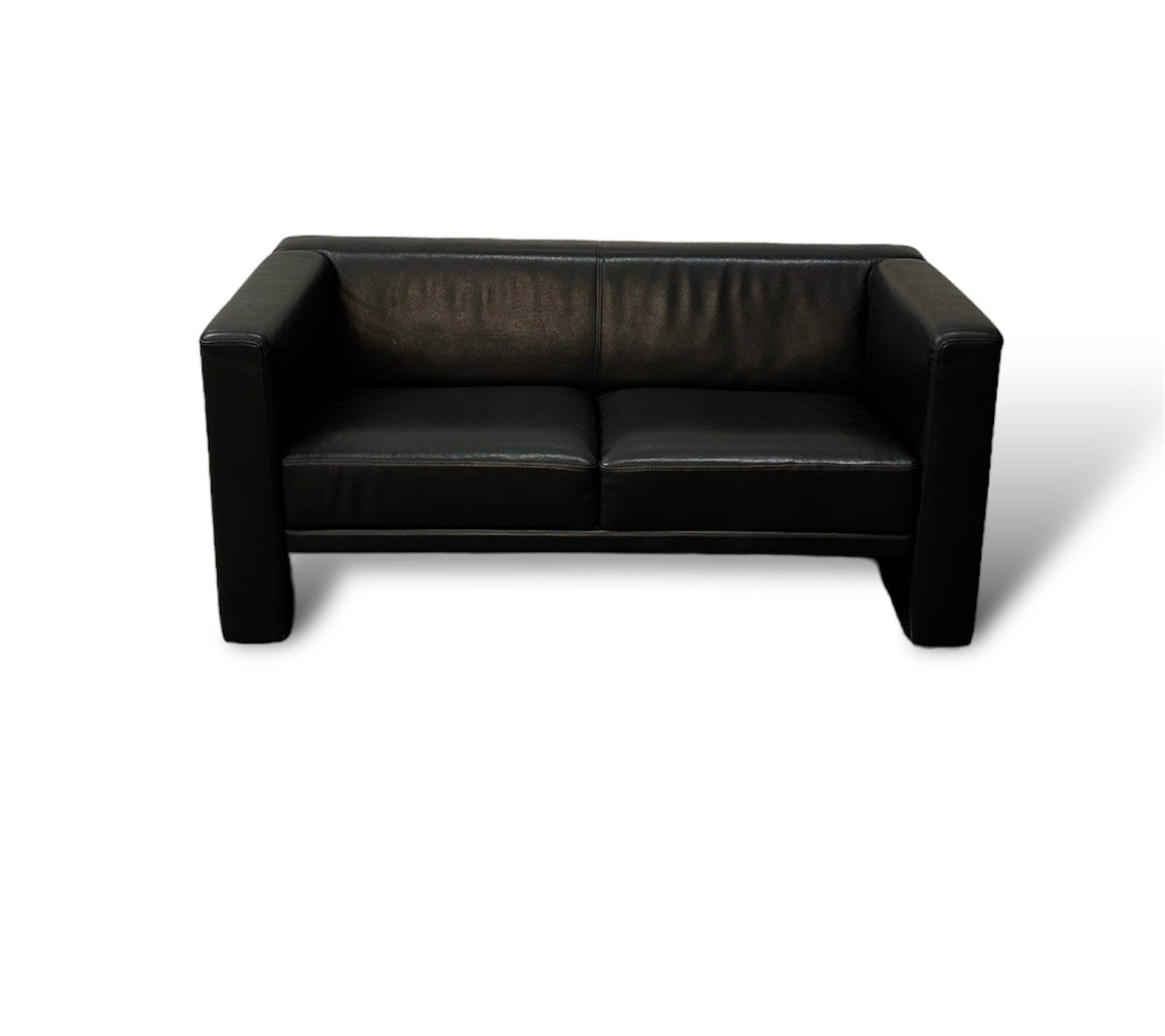 Gebrauchtes Brühl Visavis Leder Sofa in der Farbe Schwarz vor einer Wand, stilvoll und modern eingerichtet.