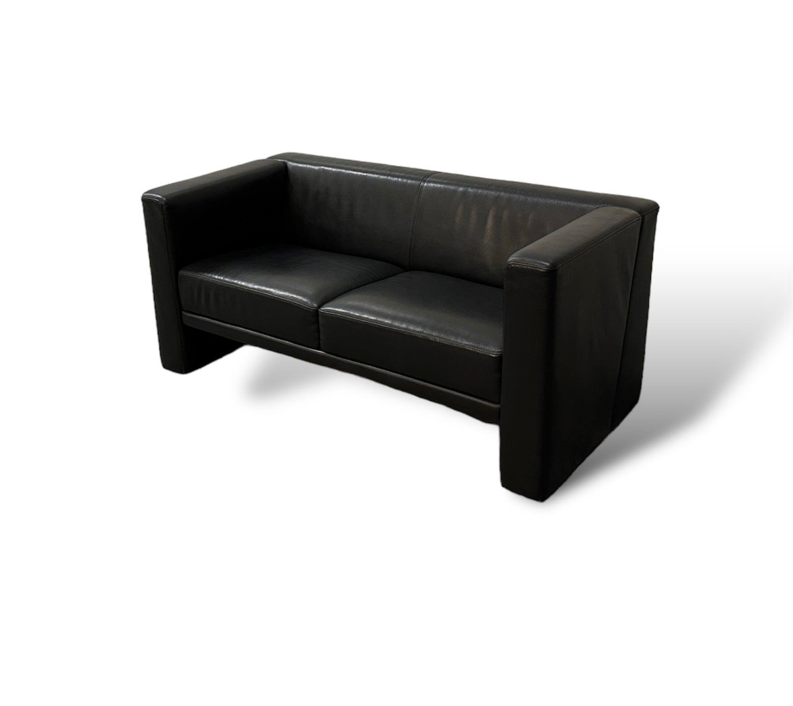 Gebrauchtes Brühl Visavis Leder Sofa in der Farbe Schwarz vor einer Wand, stilvoll und modern eingerichtet.