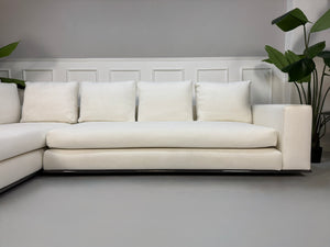 Gebrauchtes weißes Stoff Sofa Minotti Hamilton vor einer modernen Wand.