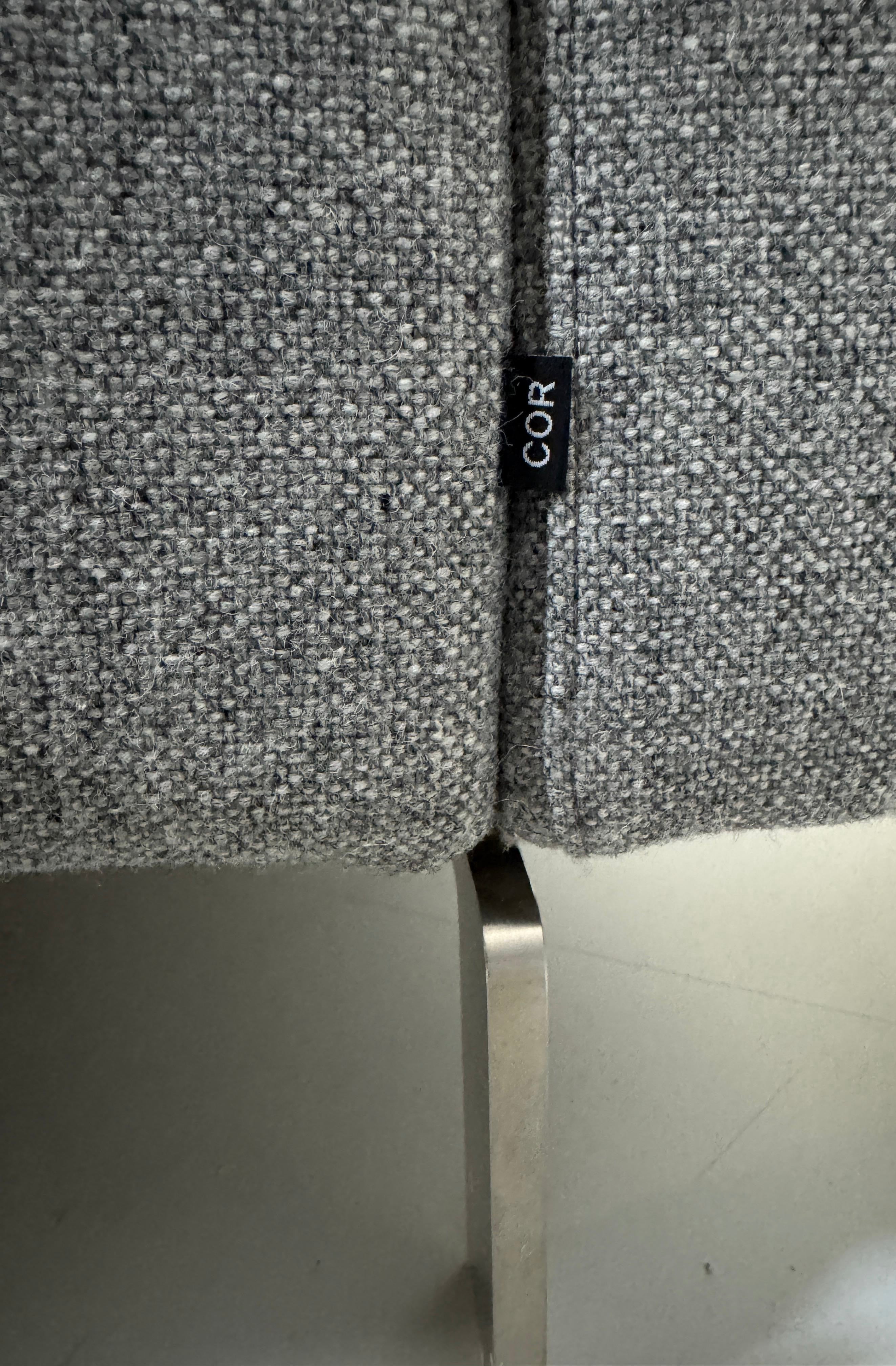 Gebrauchtes graues COR Conseta Designer Stoff Sofa vor einer Wand, stilvoll und modern eingerichtet.